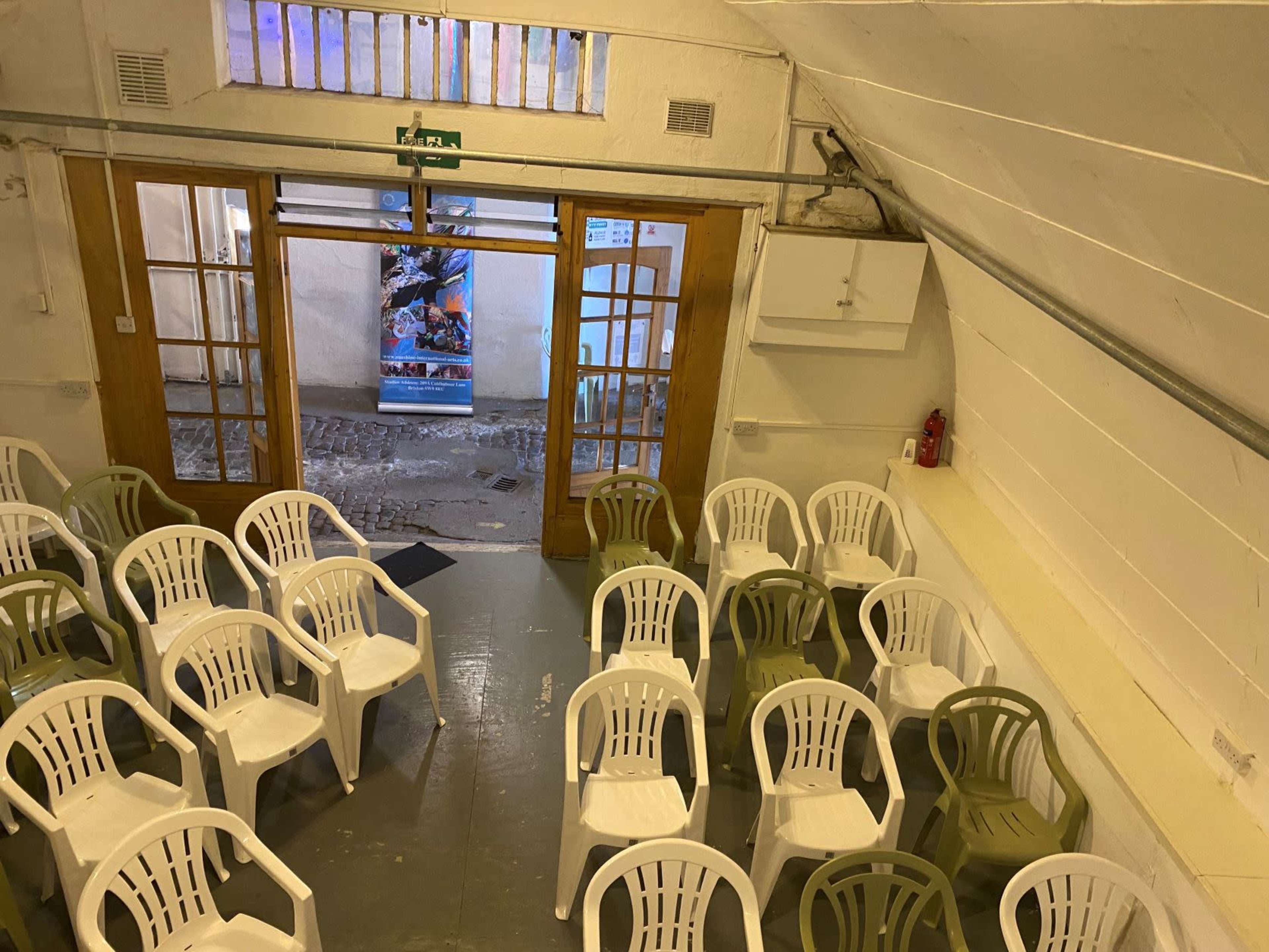 A room arranged with white and green plastic chairs facing an entrance with wooden double doors.