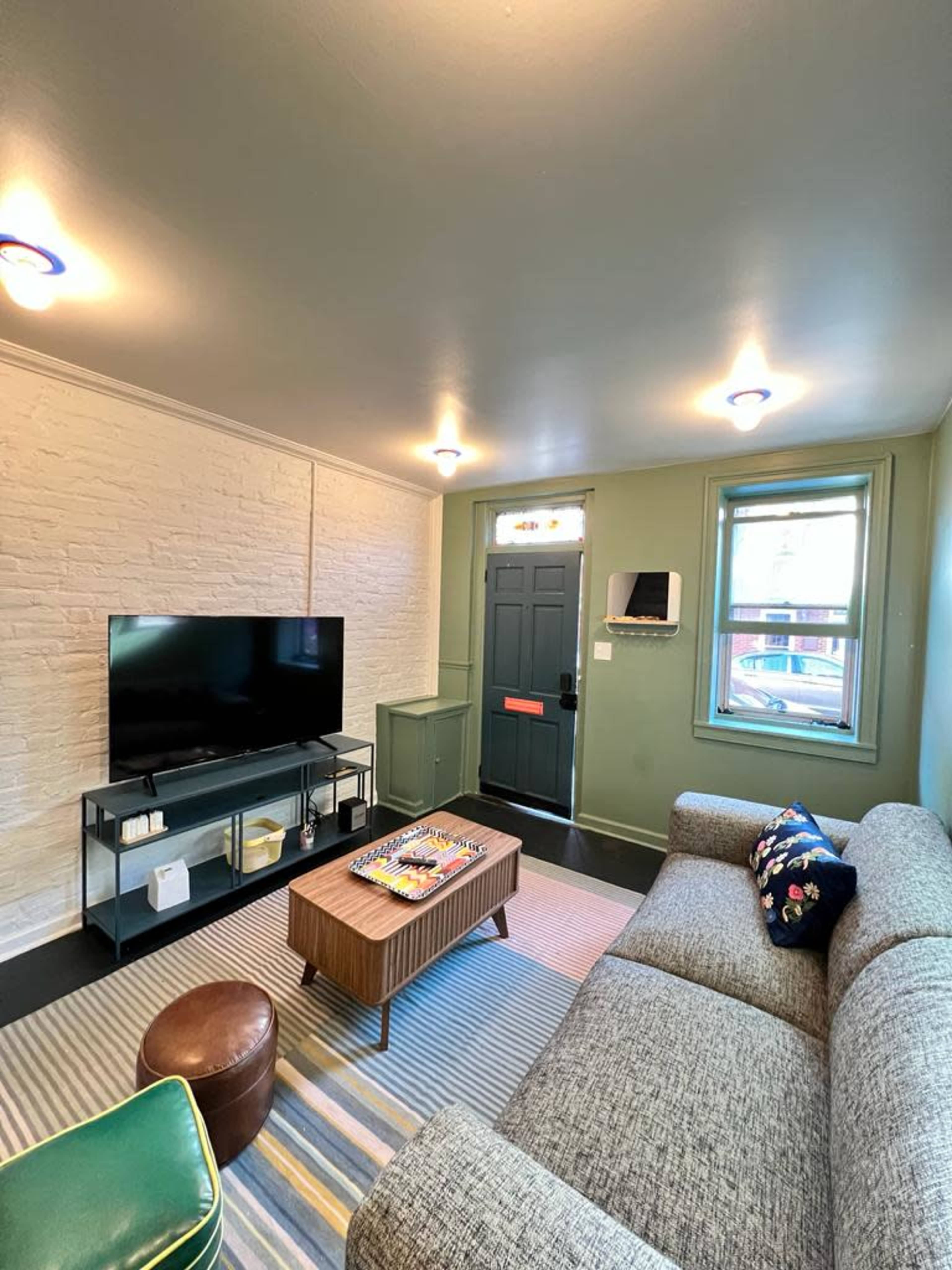 The living room features a gray sectional sofa, a wooden coffee table, a television on a glass stand, and a front door with a window.