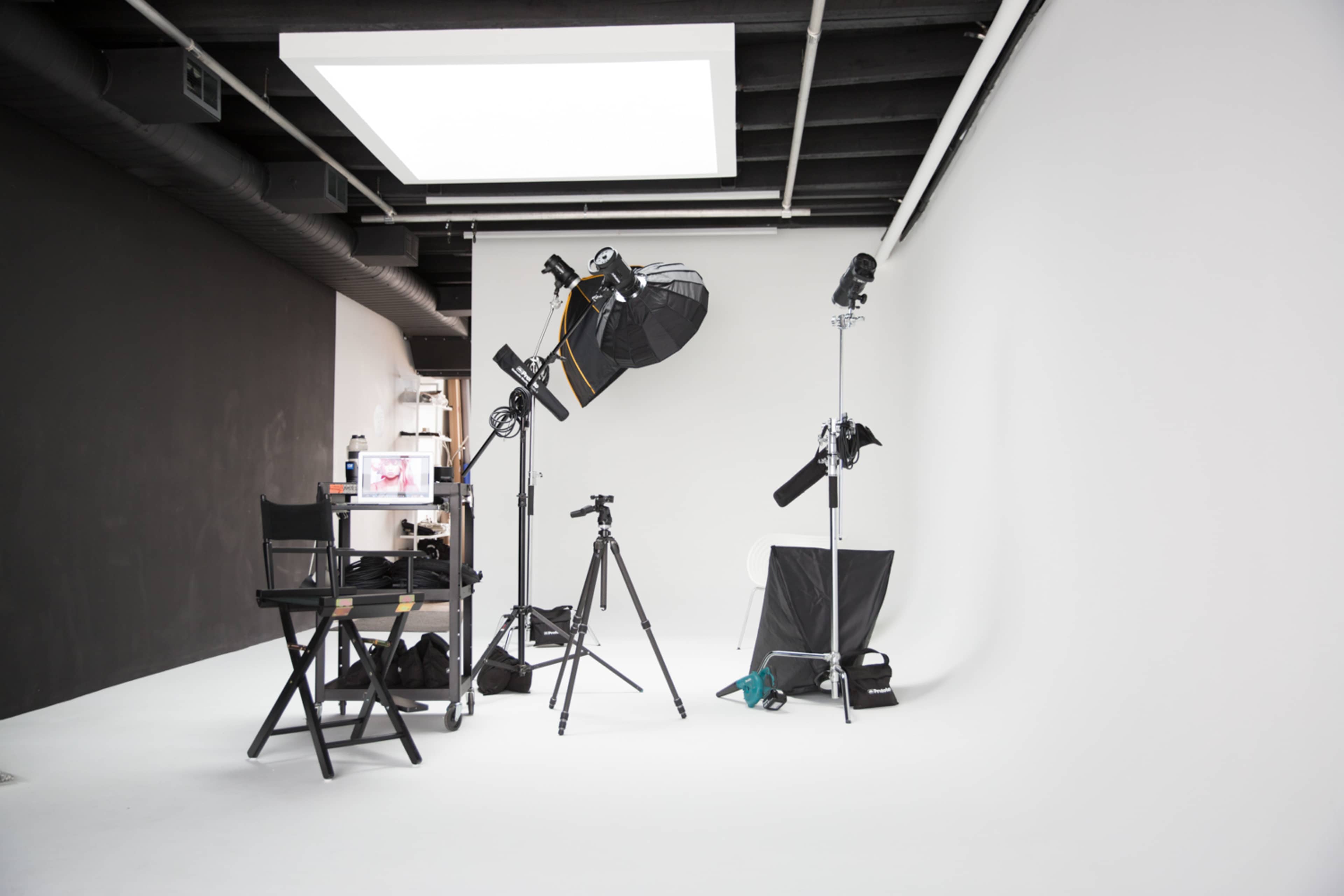 A photography studio equipped with lighting gear, tripods, a director's chair, and a blank backdrop.