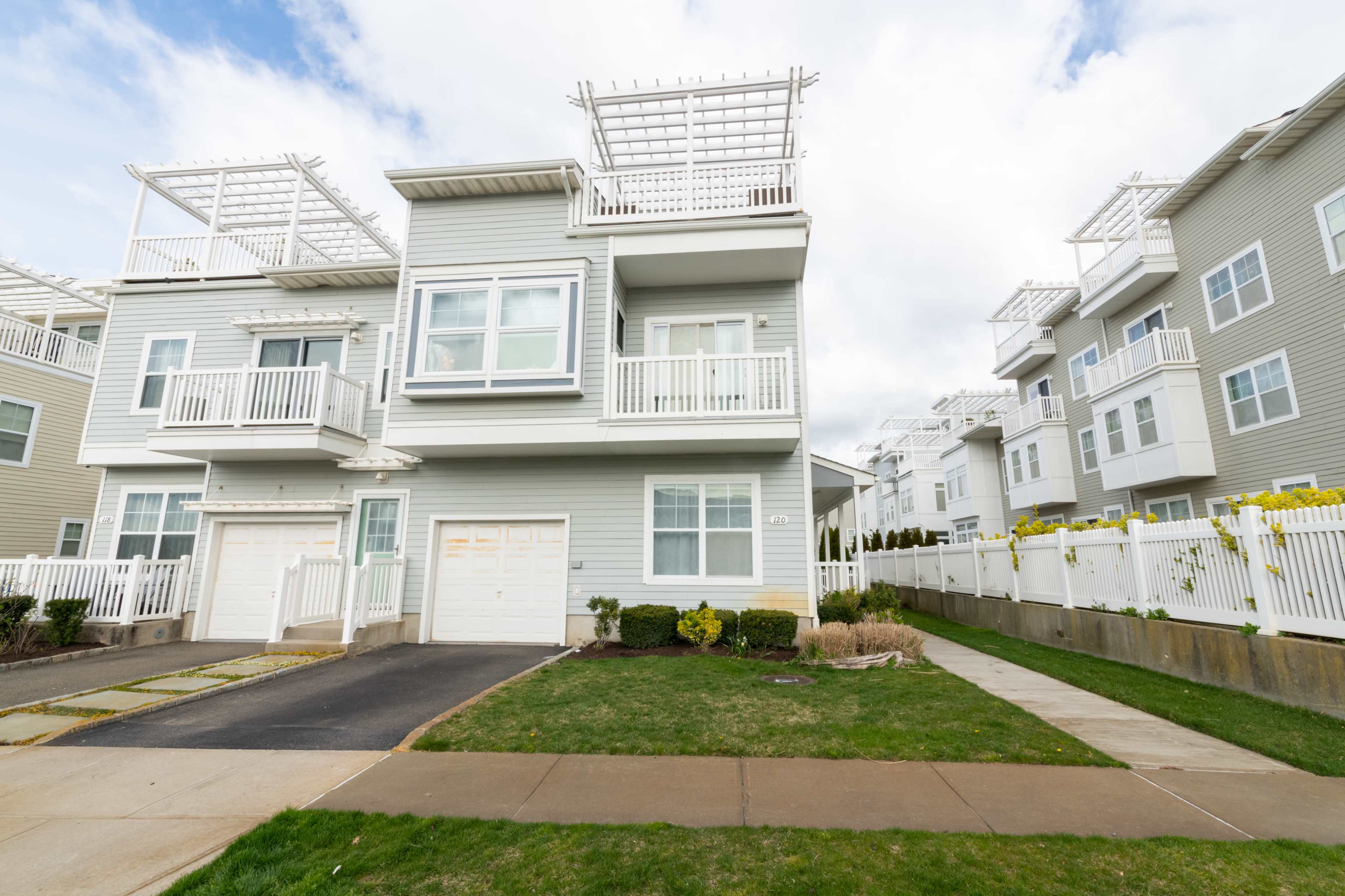 A modern two-story residential building with balconies and a garage is situated beside a paved driveway and grassy lawn.