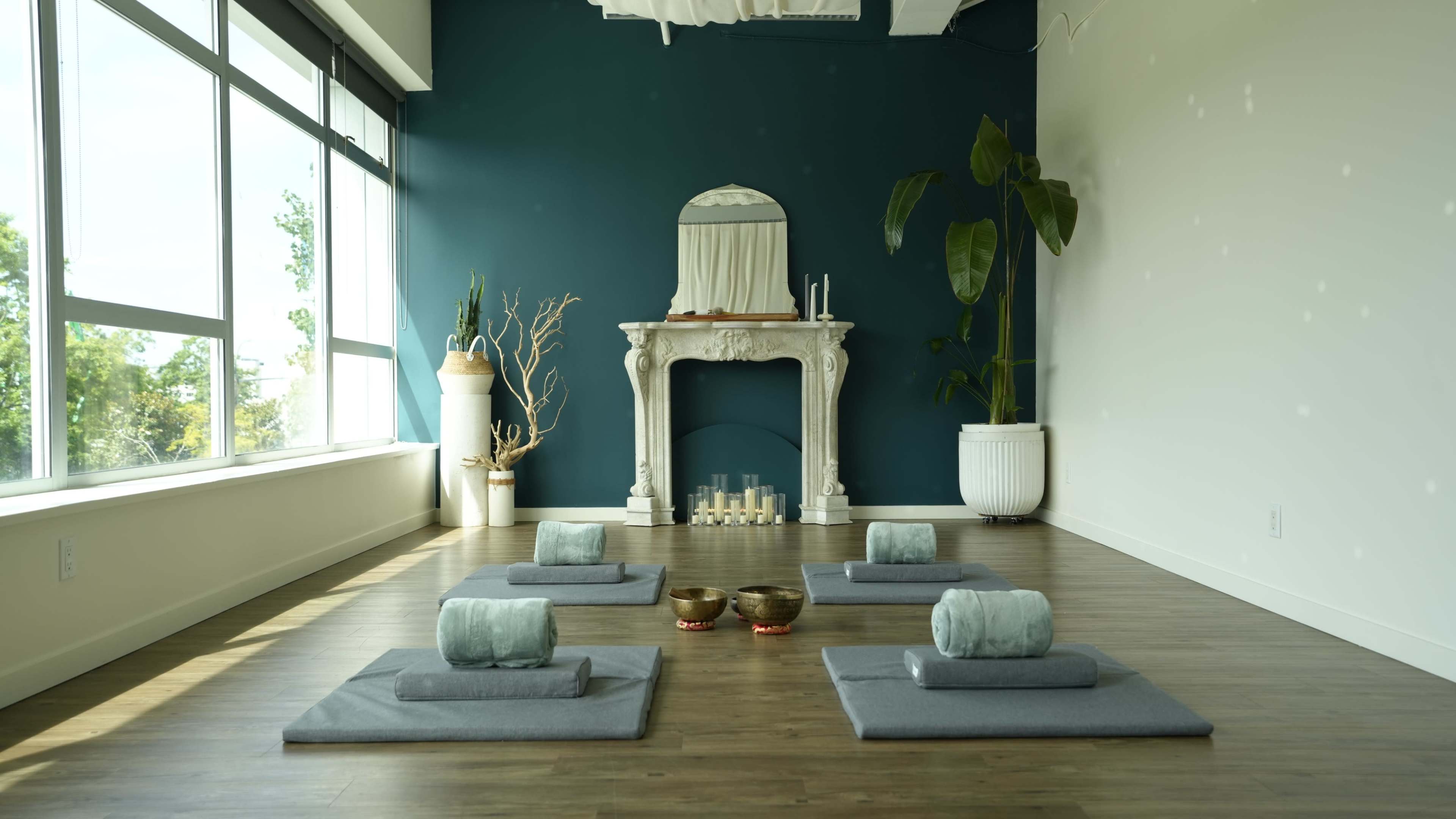 A serene yoga studio features several mats arranged on a wooden floor, with a decorative fireplace and candles in the background.