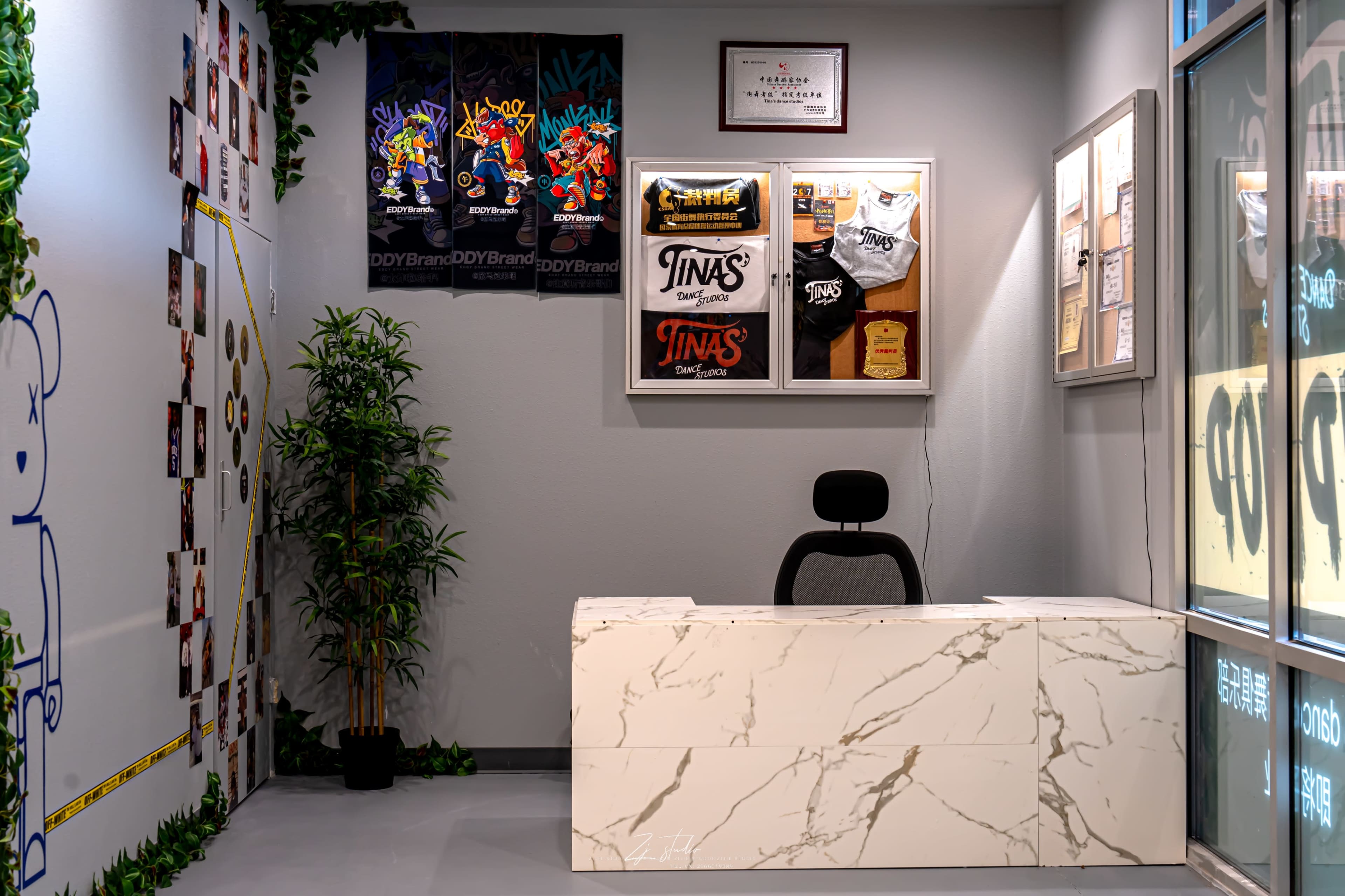 The image shows a modern reception area with a marble desk, potted plants, and framed clothing designs on the wall.