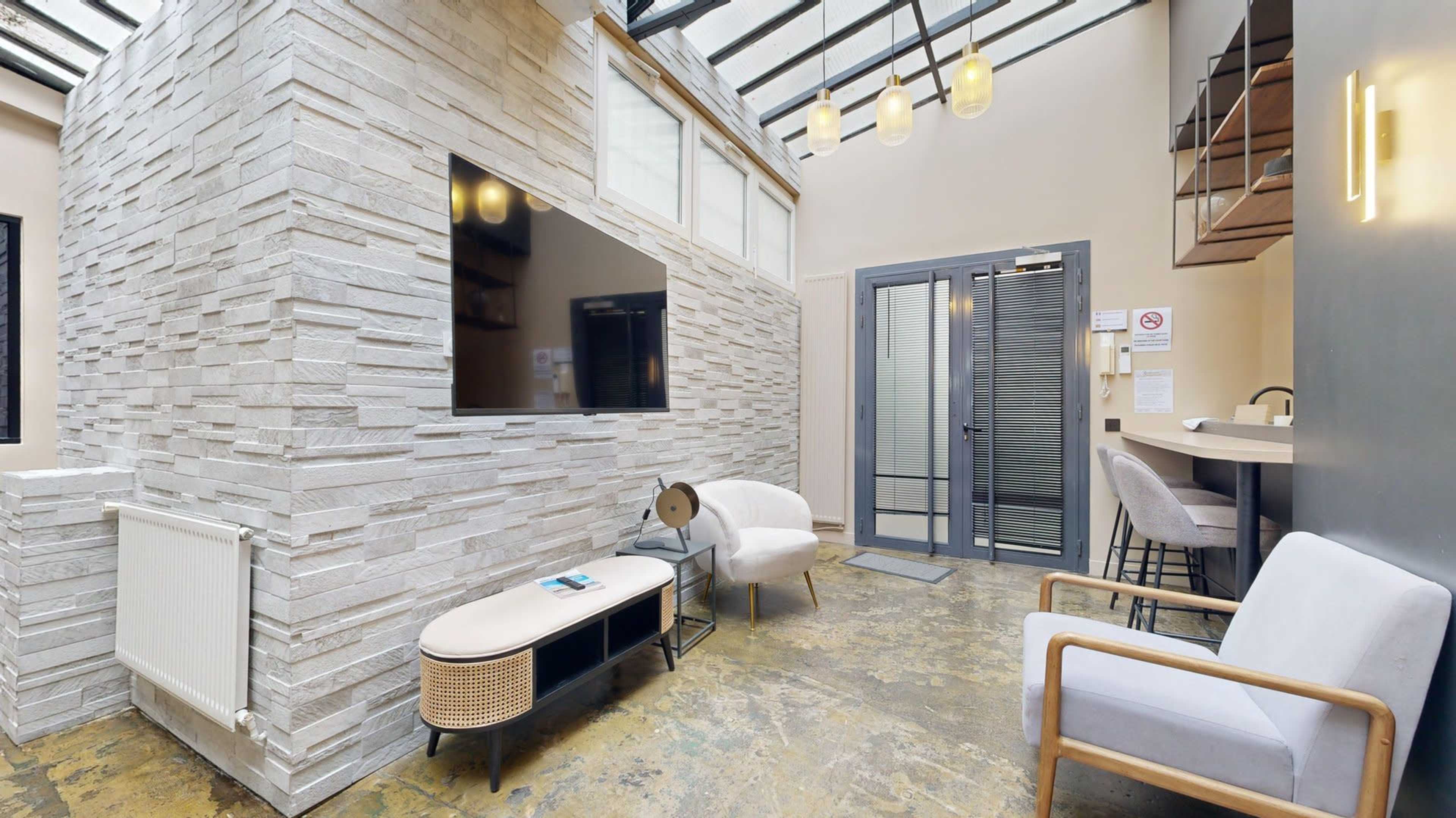 The image shows a modern interior space featuring a stone wall, a television, a seating area, and a bar-style counter with high chairs.