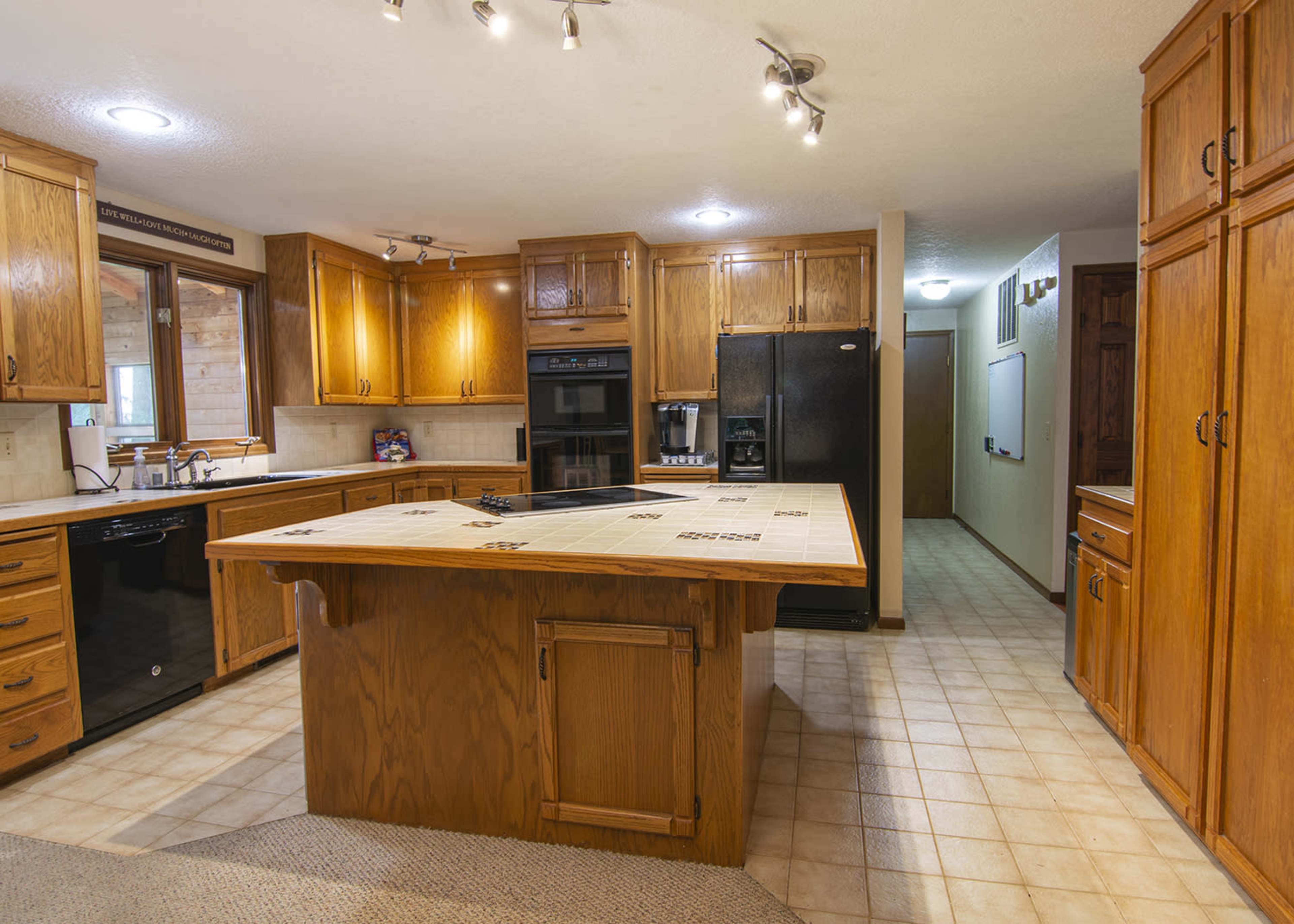 A spacious kitchen with wooden cabinets, a central island with a tile countertop, and black appliances.