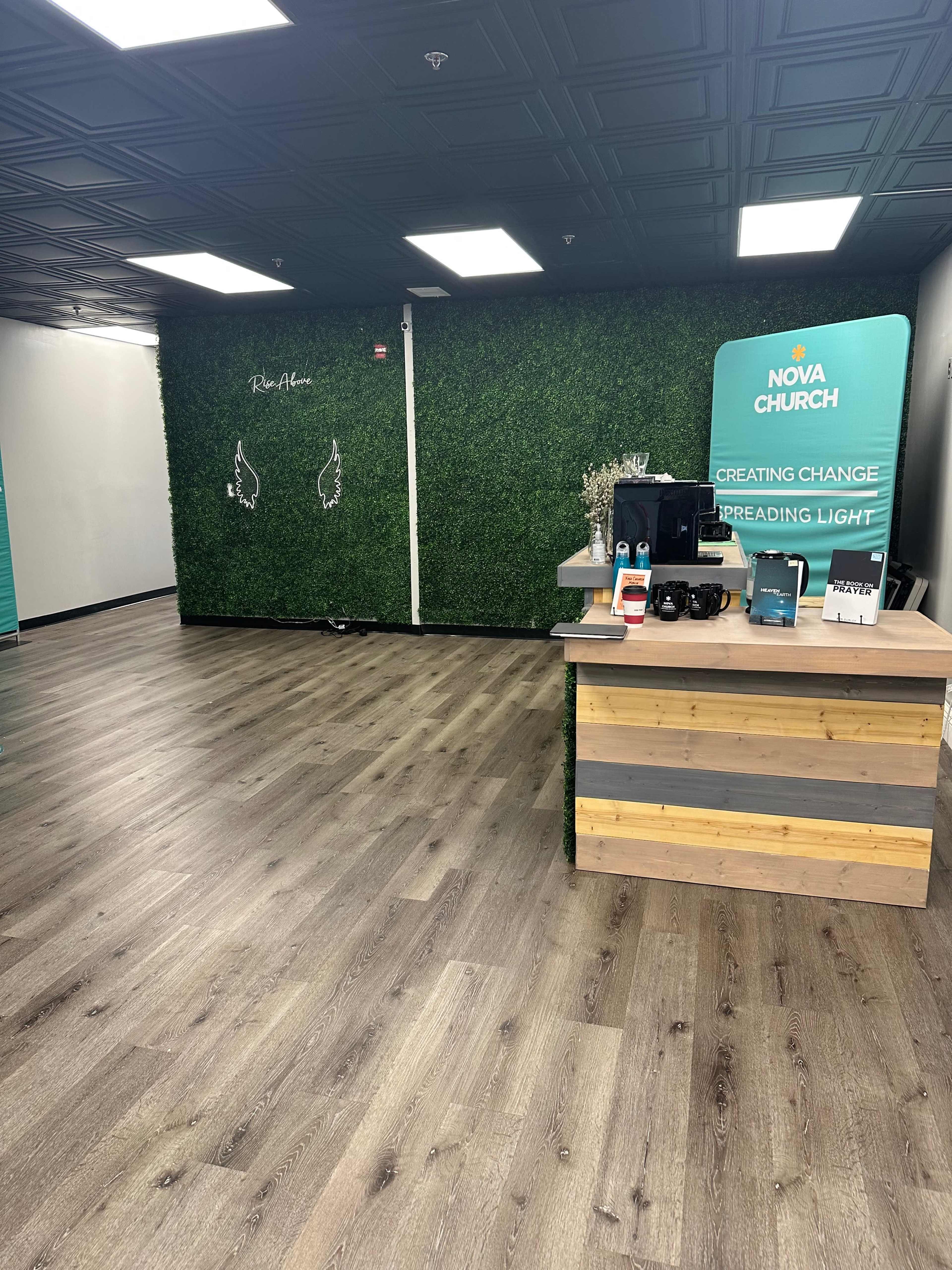 The interior of a modern church space features a wooden reception desk, a green accent wall with artificial grass, and a minimalistic layout with wooden flooring.