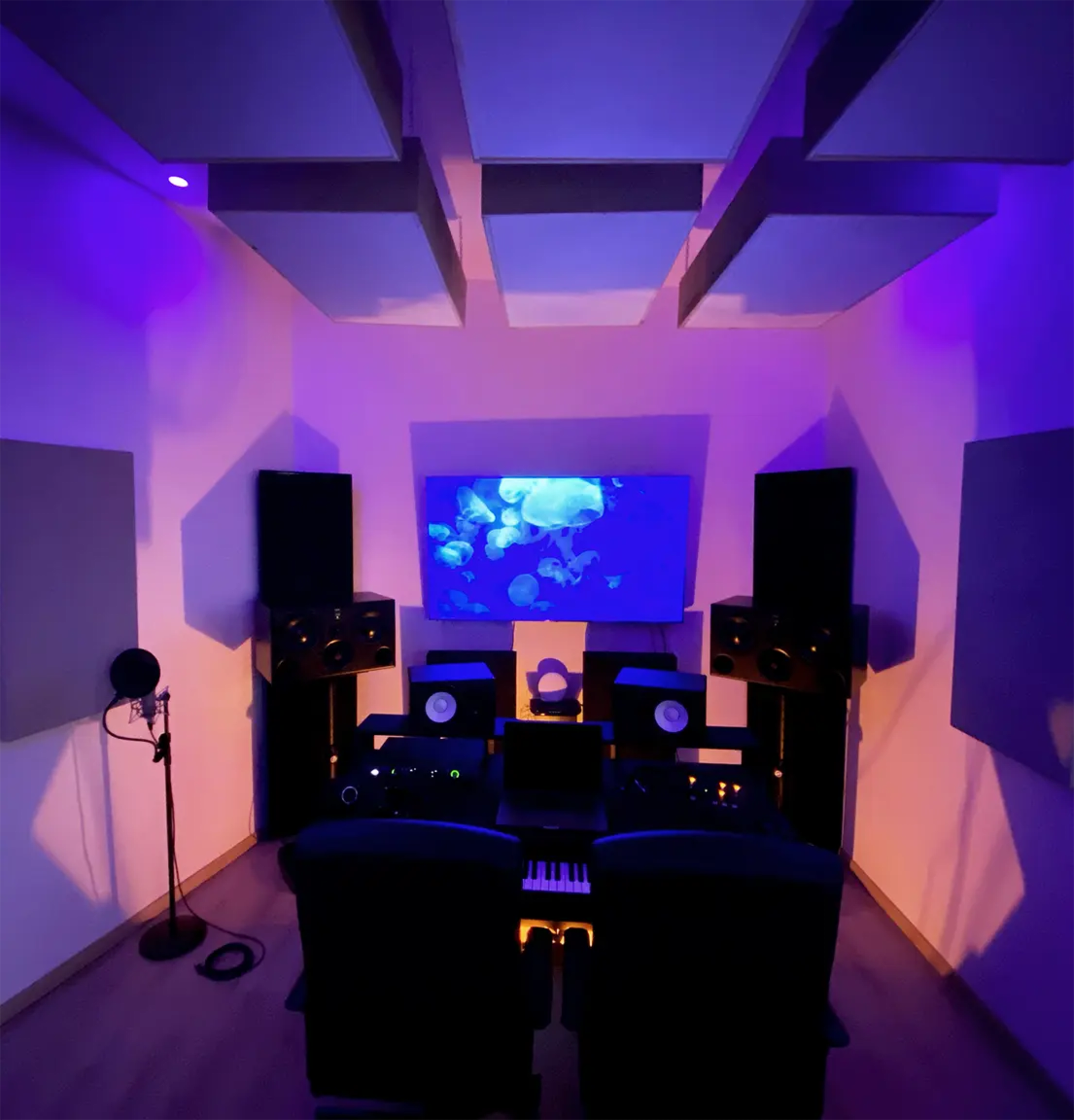 A music studio featuring two chairs facing a console surrounded by large speakers, acoustic panels, and a projected video of jellyfish on the wall.