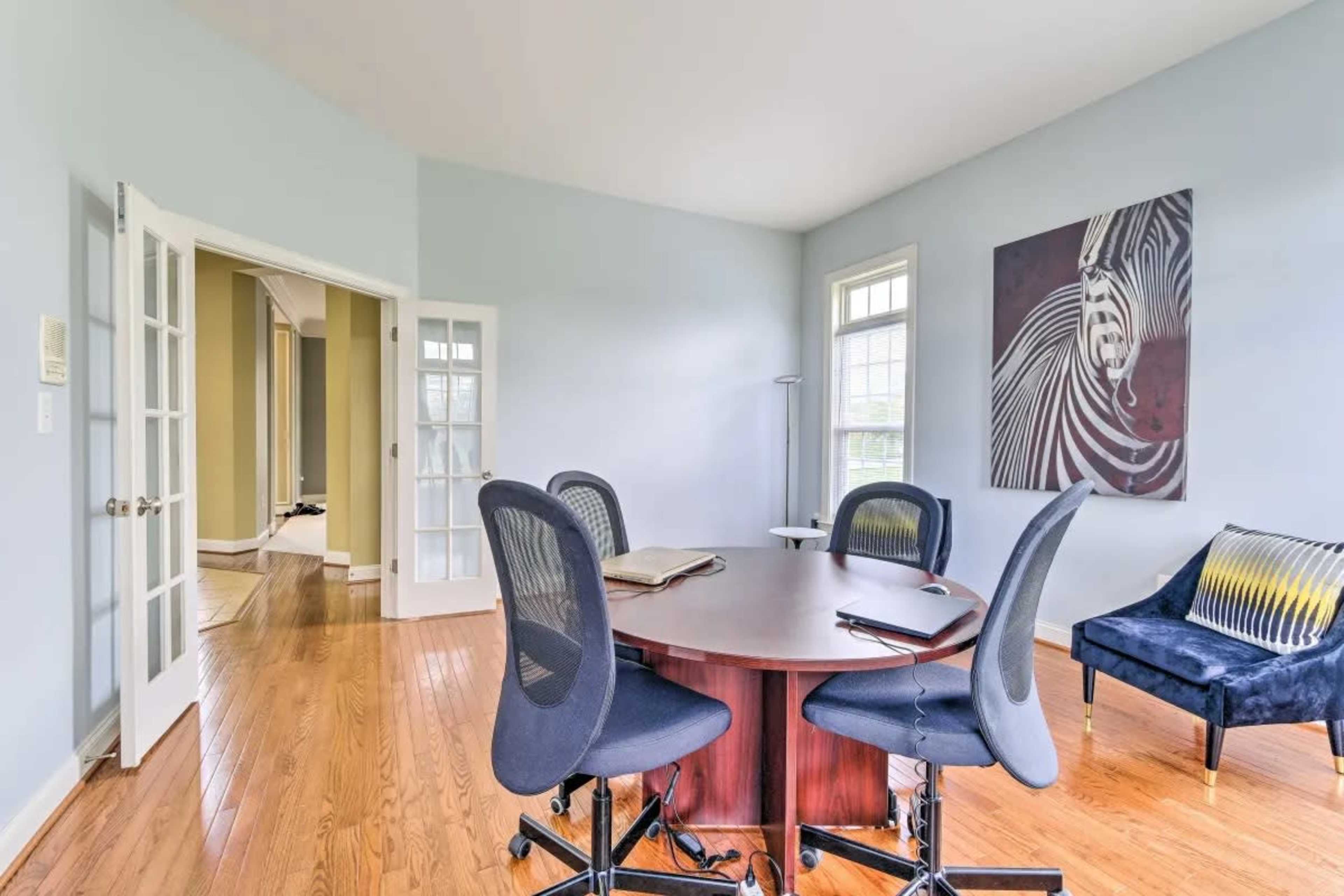A meeting room with a round table surrounded by four chairs, a blue accent wall, and a large piece of abstract art on the wall.