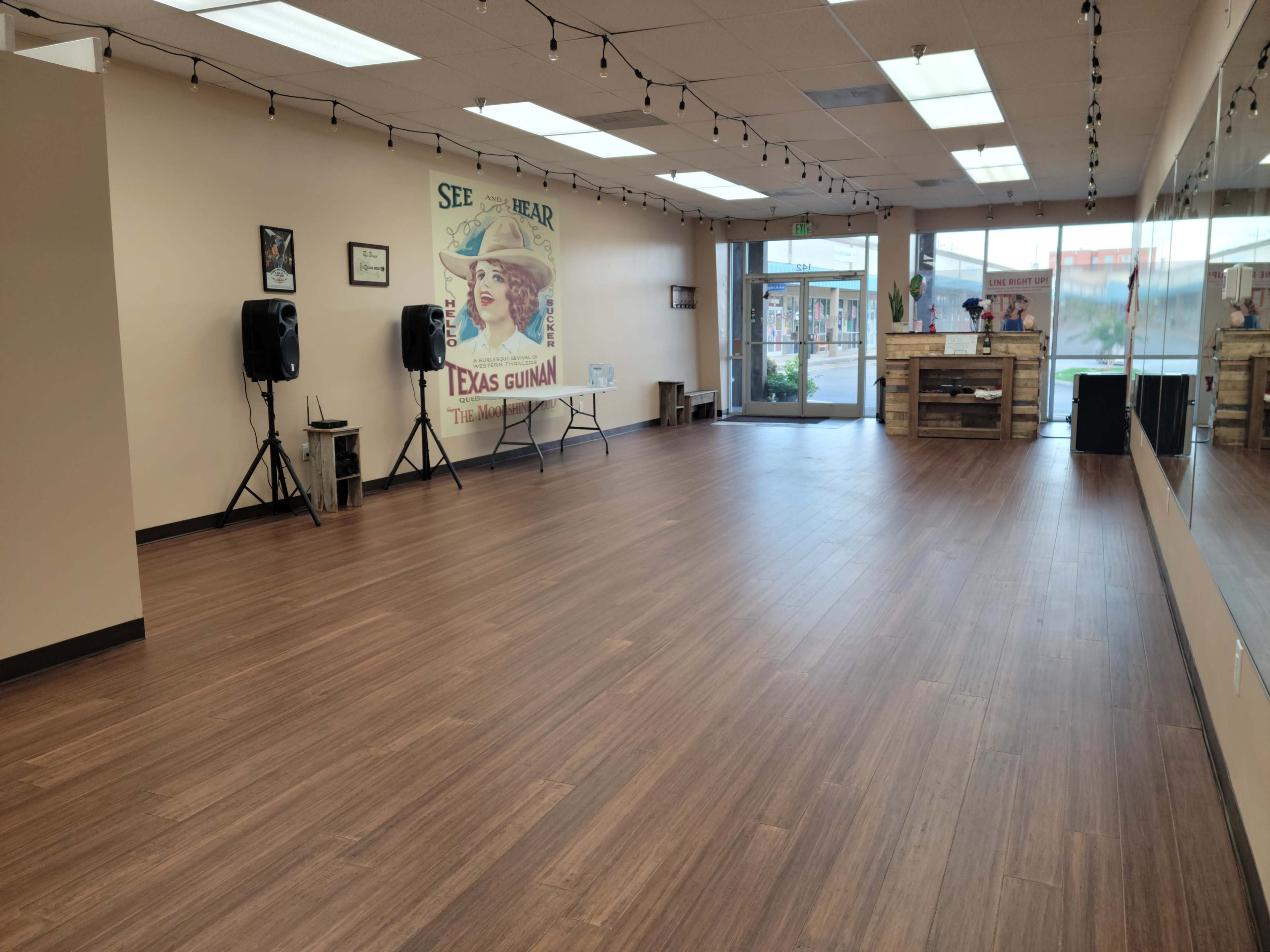 A spacious, empty studio with wooden flooring, featuring a large window at one end and a poster on the wall.