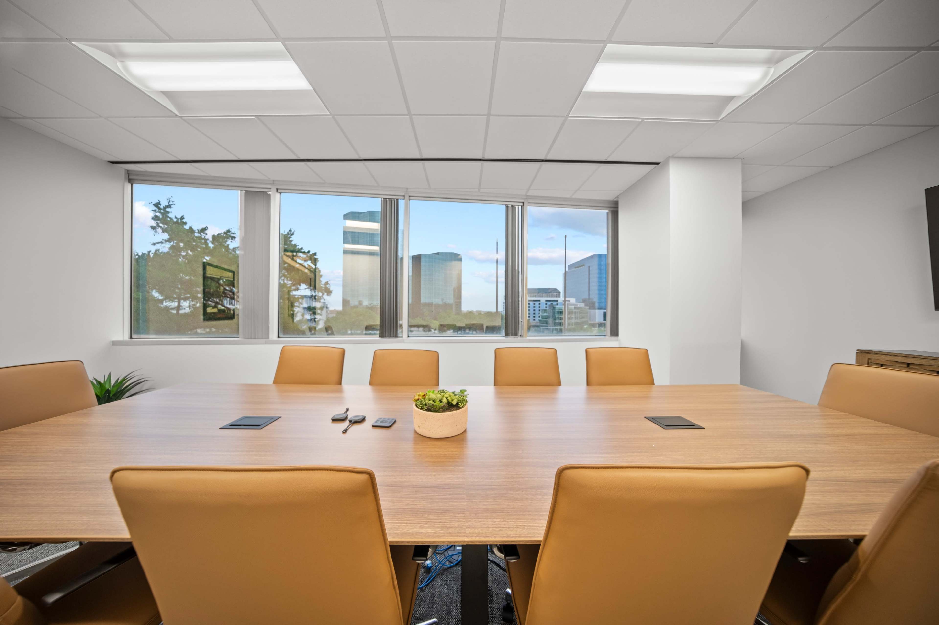 A large conference room features a wooden table surrounded by brown leather chairs, with large windows offering a view of city buildings.