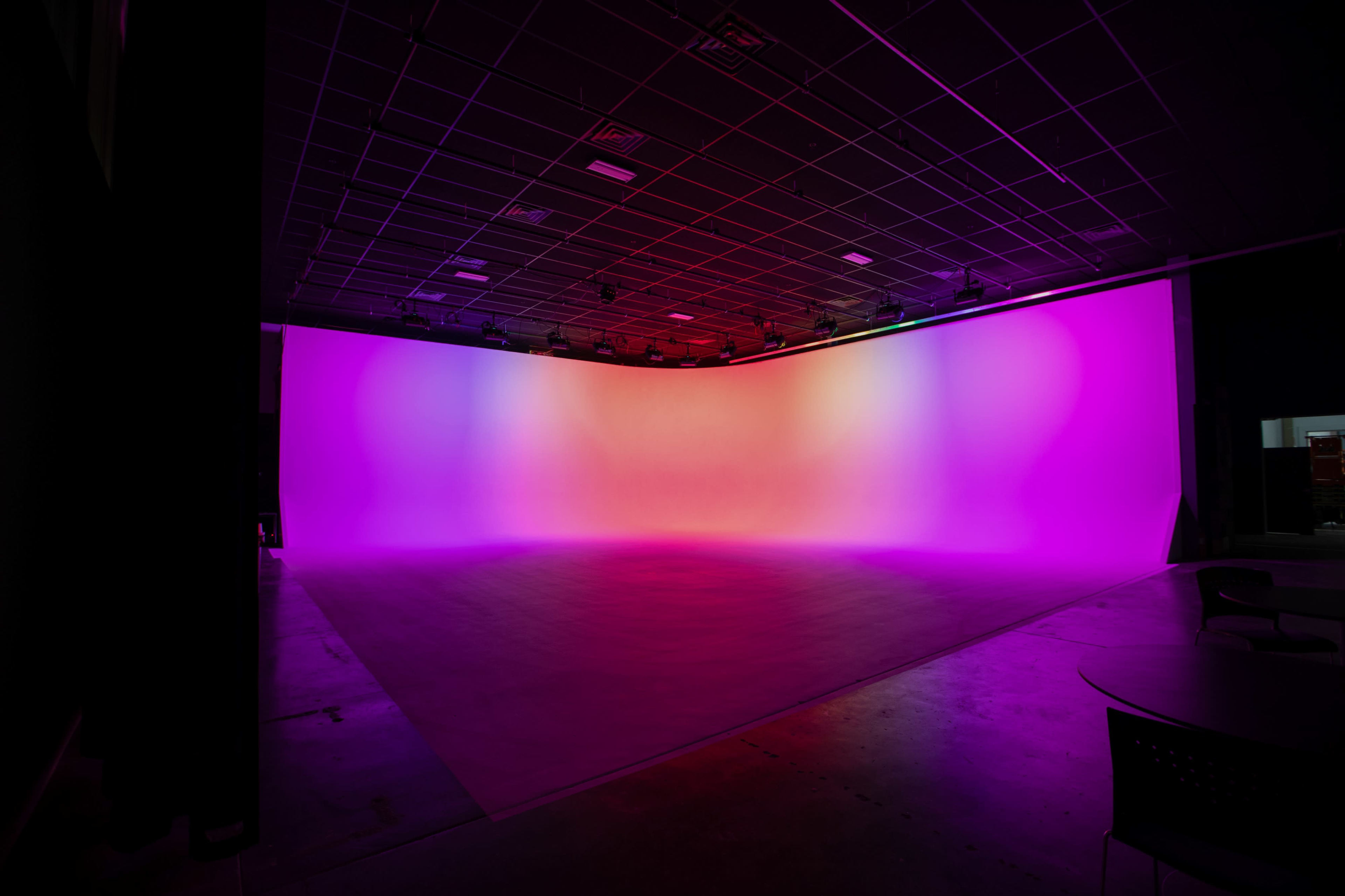 A large studio space features a curved backdrop illuminated with gradient colors from pink to orange.