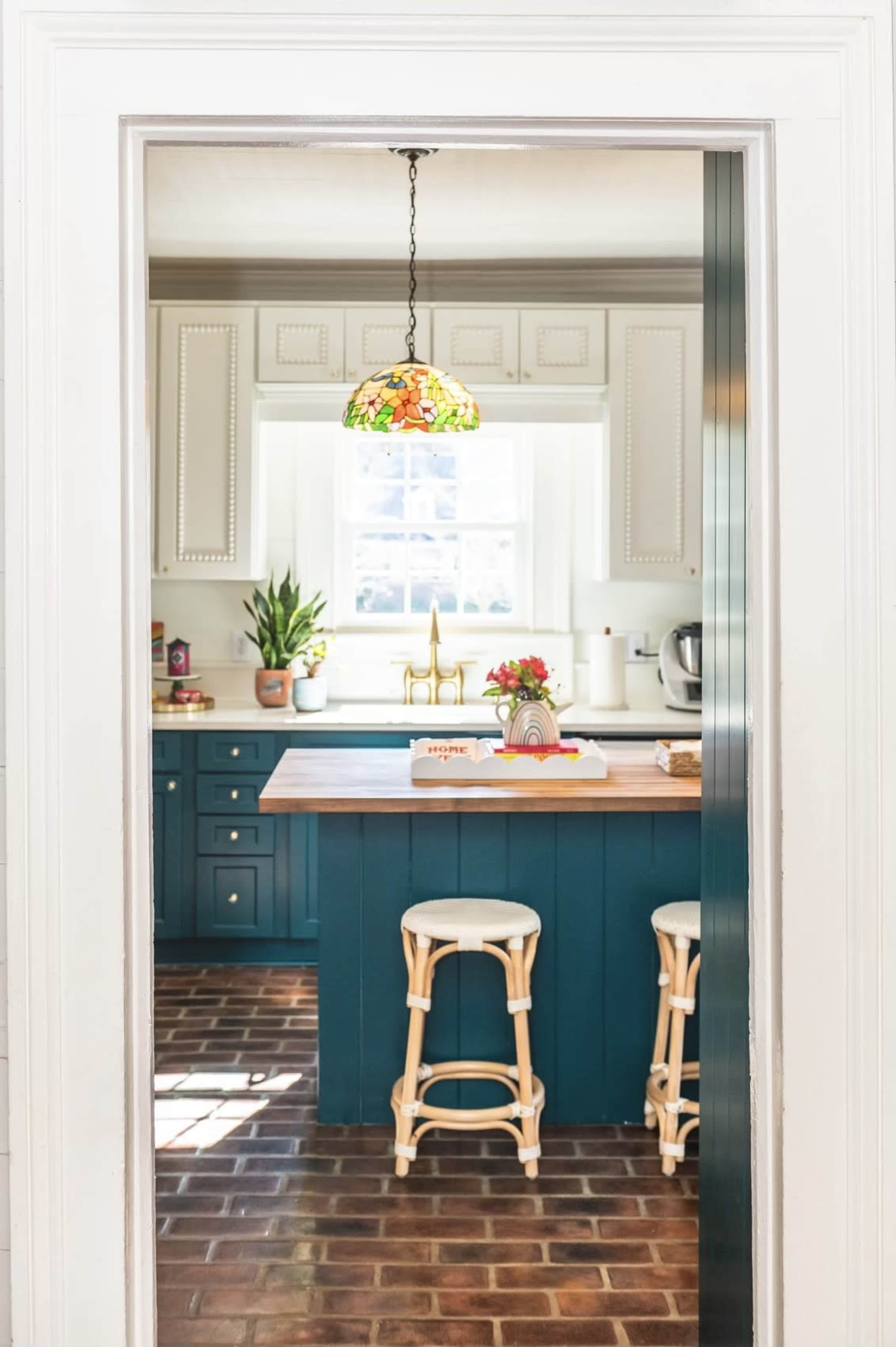 A doorway frames a colorful kitchen featuring a central island with two bar stools and a decorative pendant light hanging above.