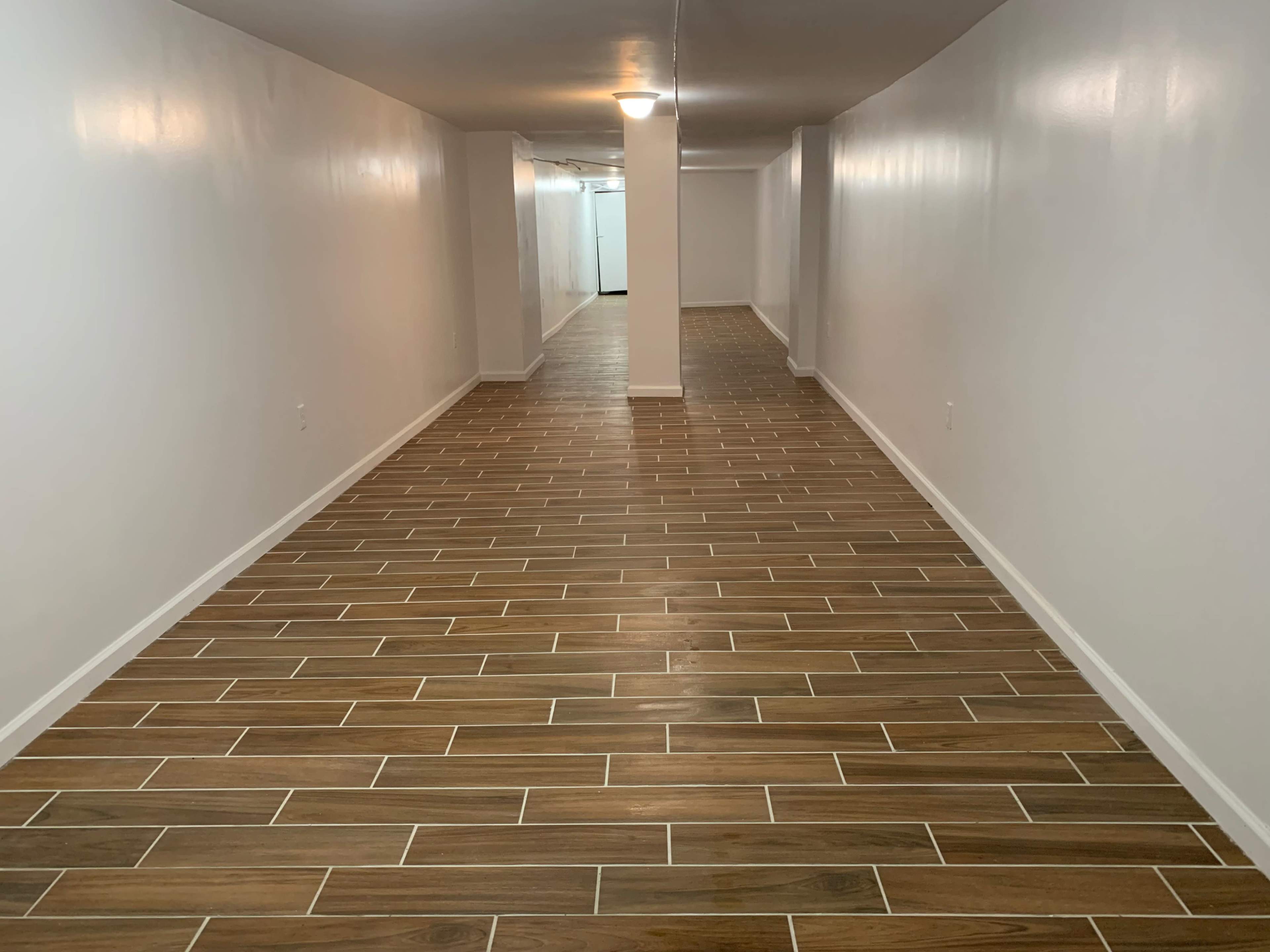 A long, narrow hallway with polished brown tile flooring and white walls.