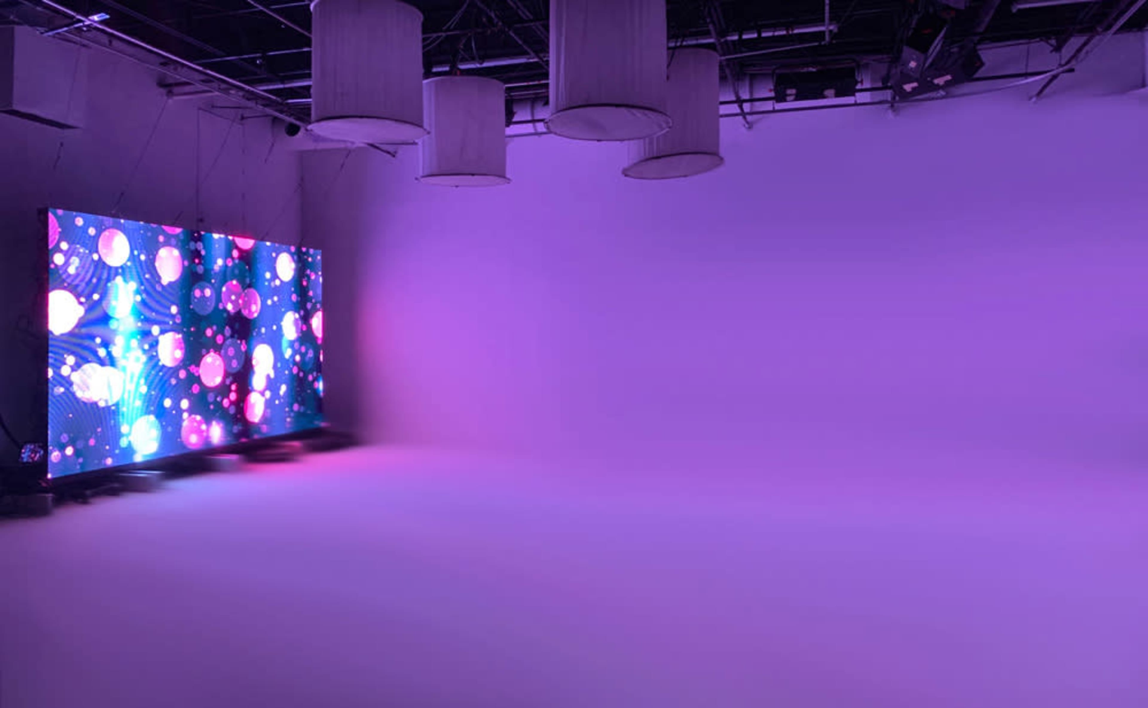 A brightly lit studio features a large screen displaying colorful abstract patterns against a plain purple background.
