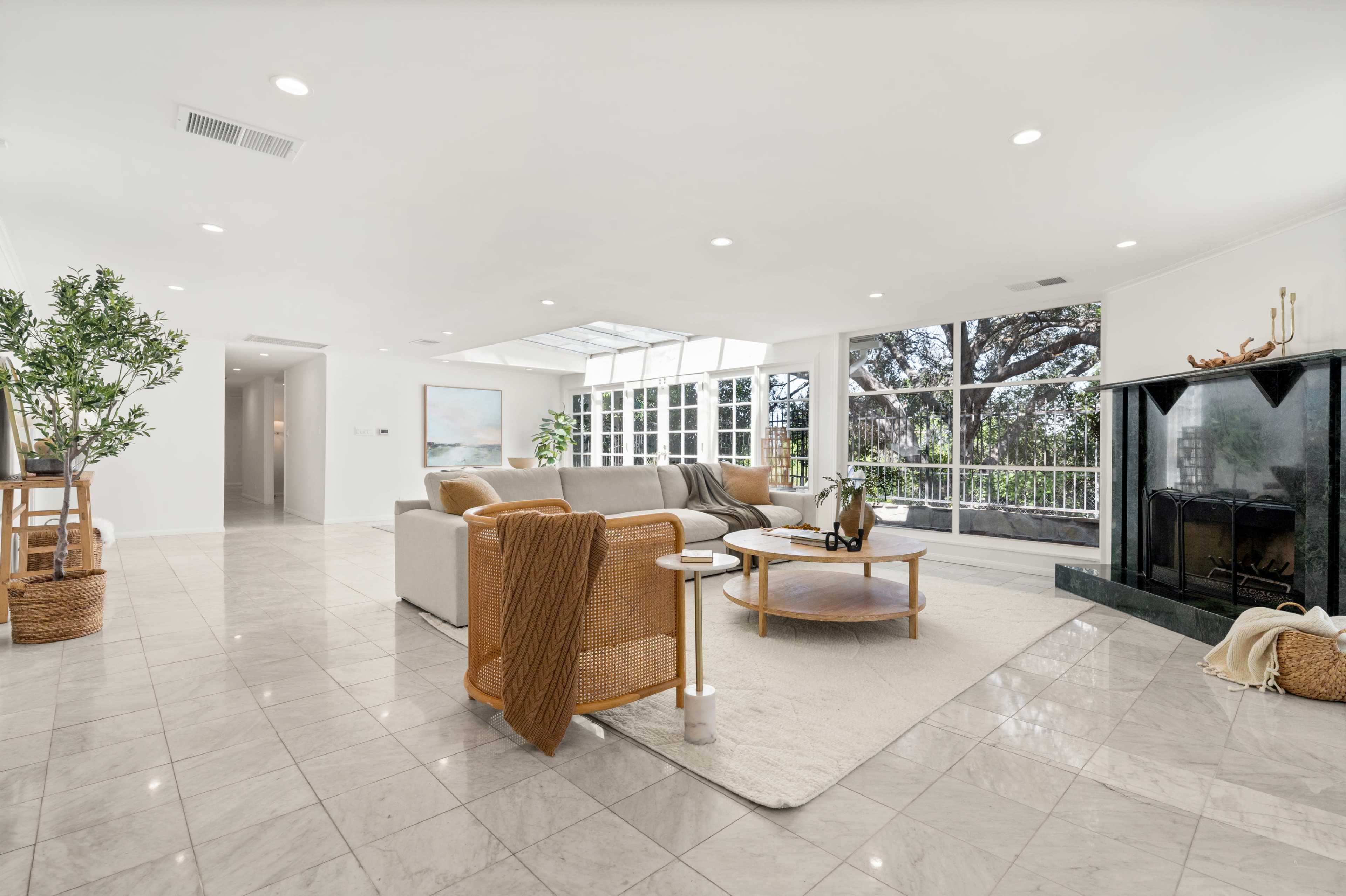 The spacious living room features large windows, a tiled floor, and a fireplace with modern furniture arranged for relaxation.