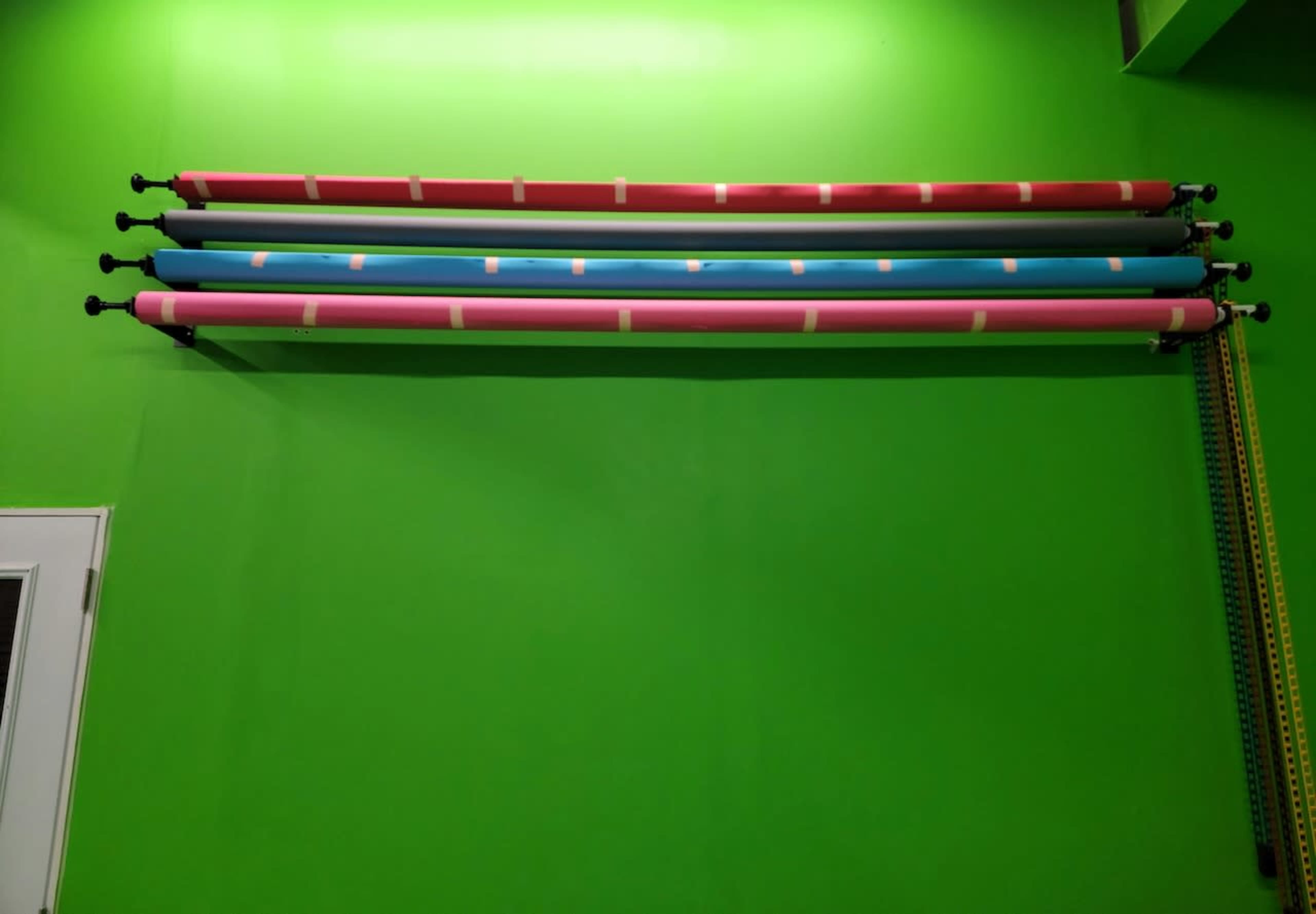 Four rolls of colored backdrop paper are mounted on a bright green wall.