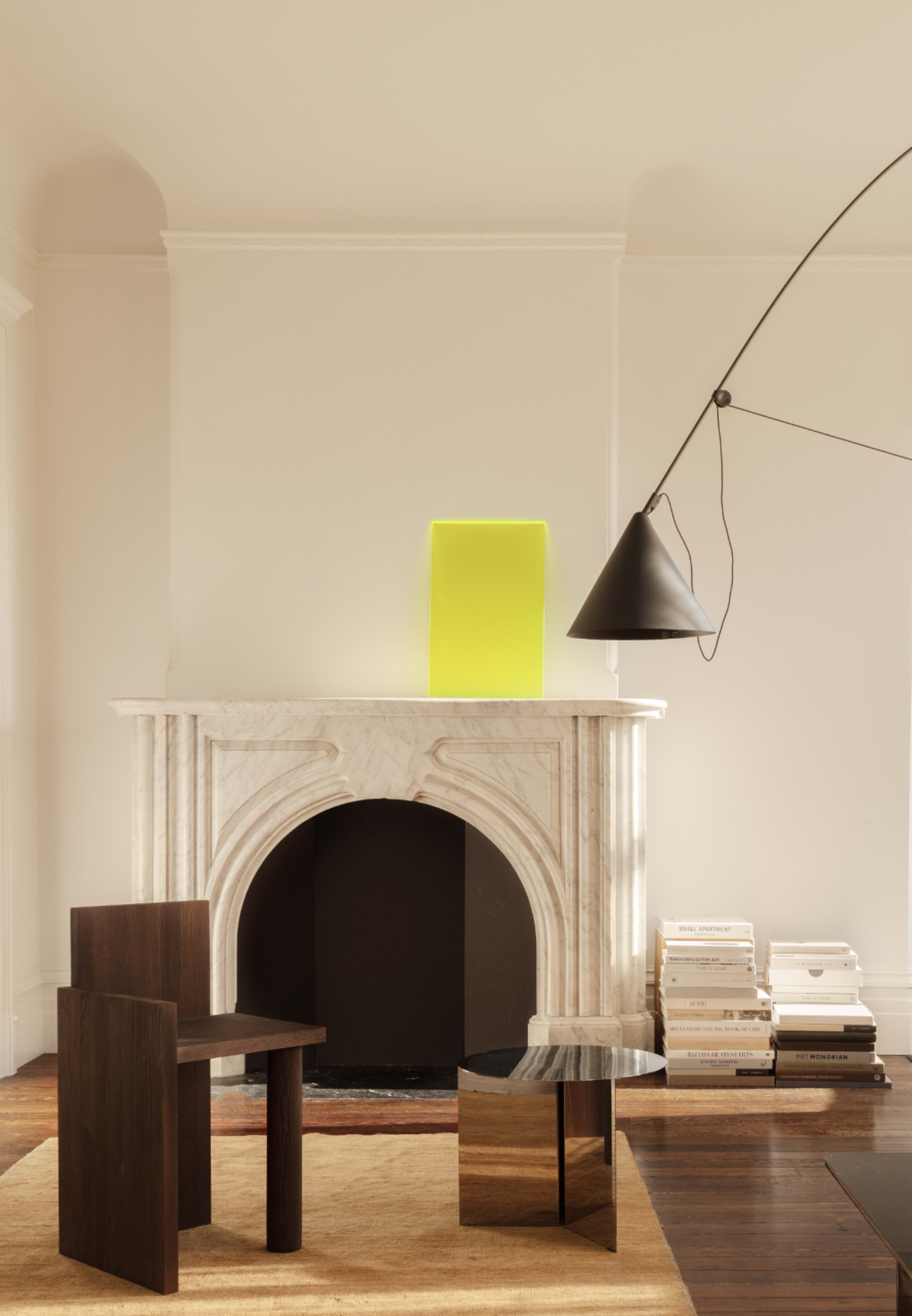 A modern living room featuring a marble fireplace, a yellow rectangular lamp on the mantle, and a black chair and table in front of it.