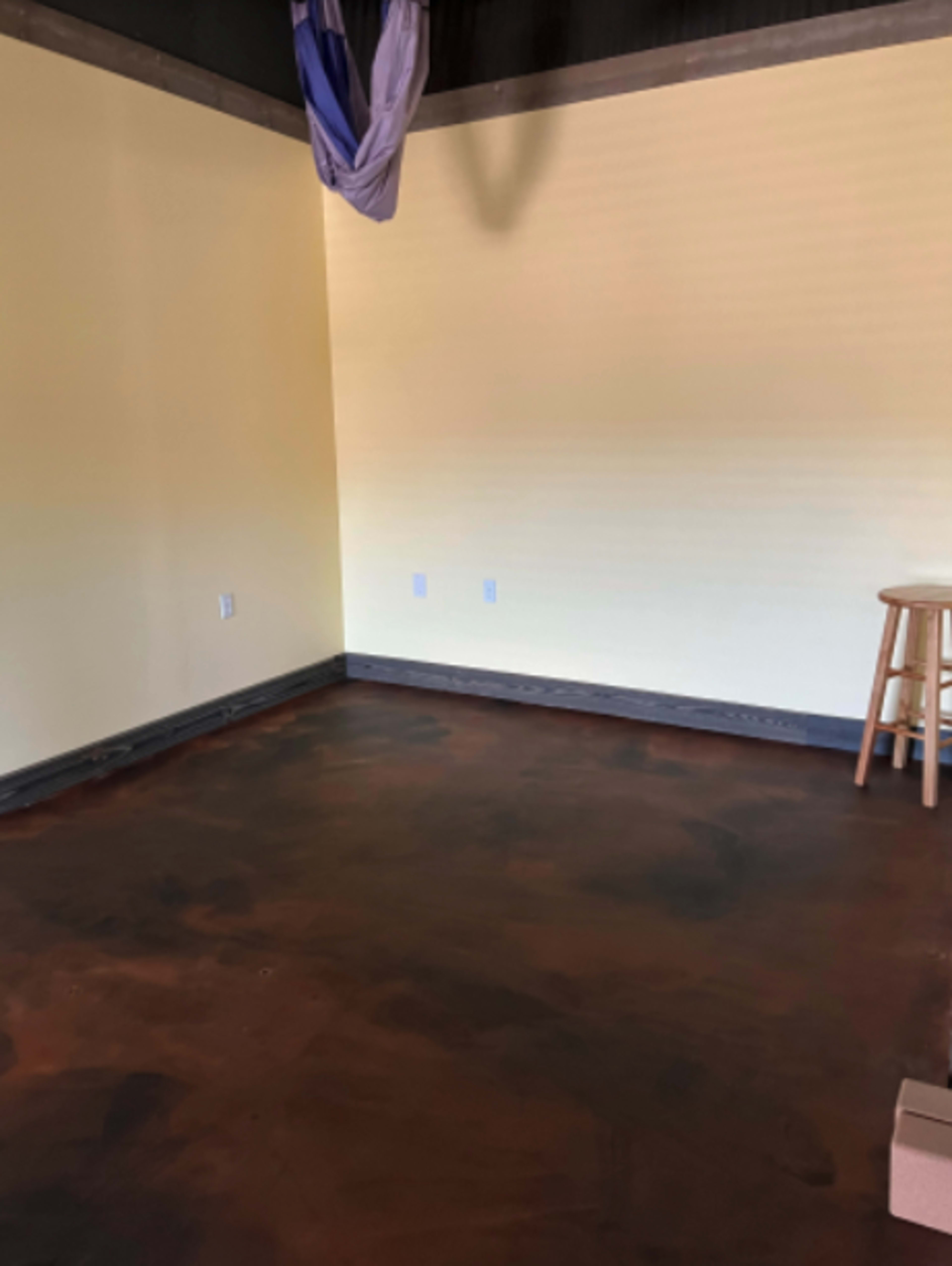 An empty room with yellow walls, a brown floor, and a wooden stool in one corner.