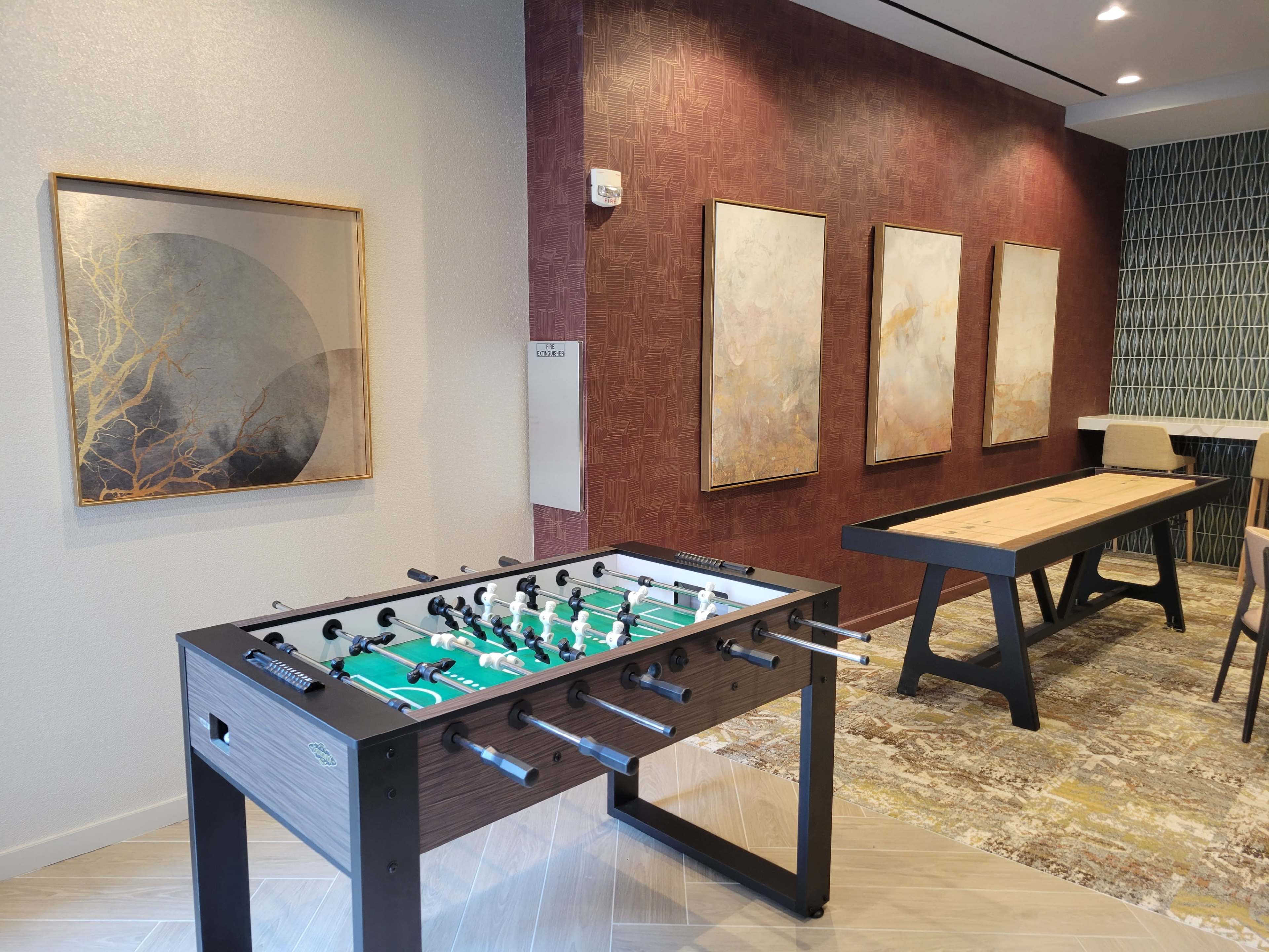 A foosball table beside a dining table, with framed artwork on the wall in a spacious room.