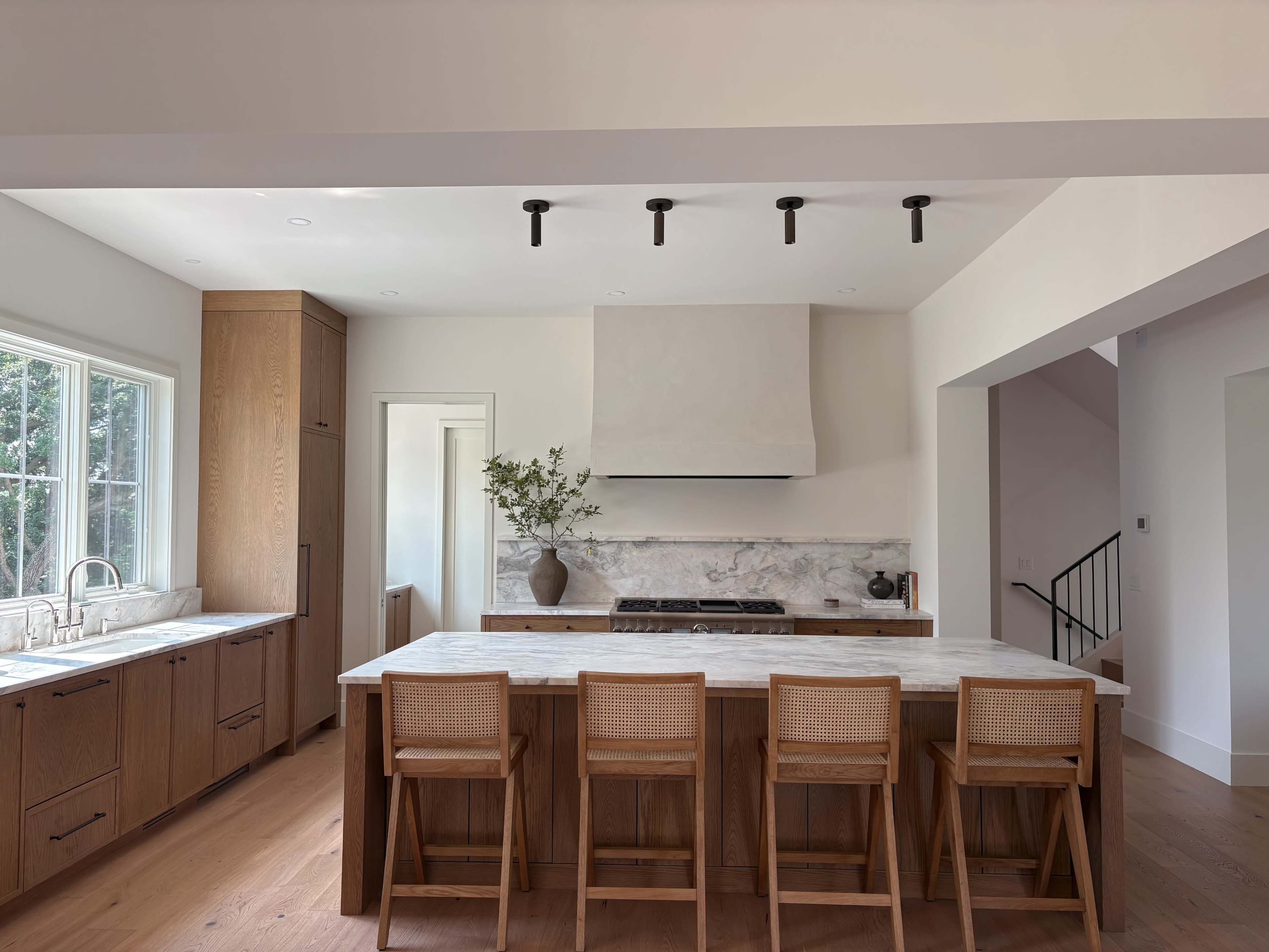The image depicts a modern kitchen with wooden cabinetry, a large marble island, and a white range hood.