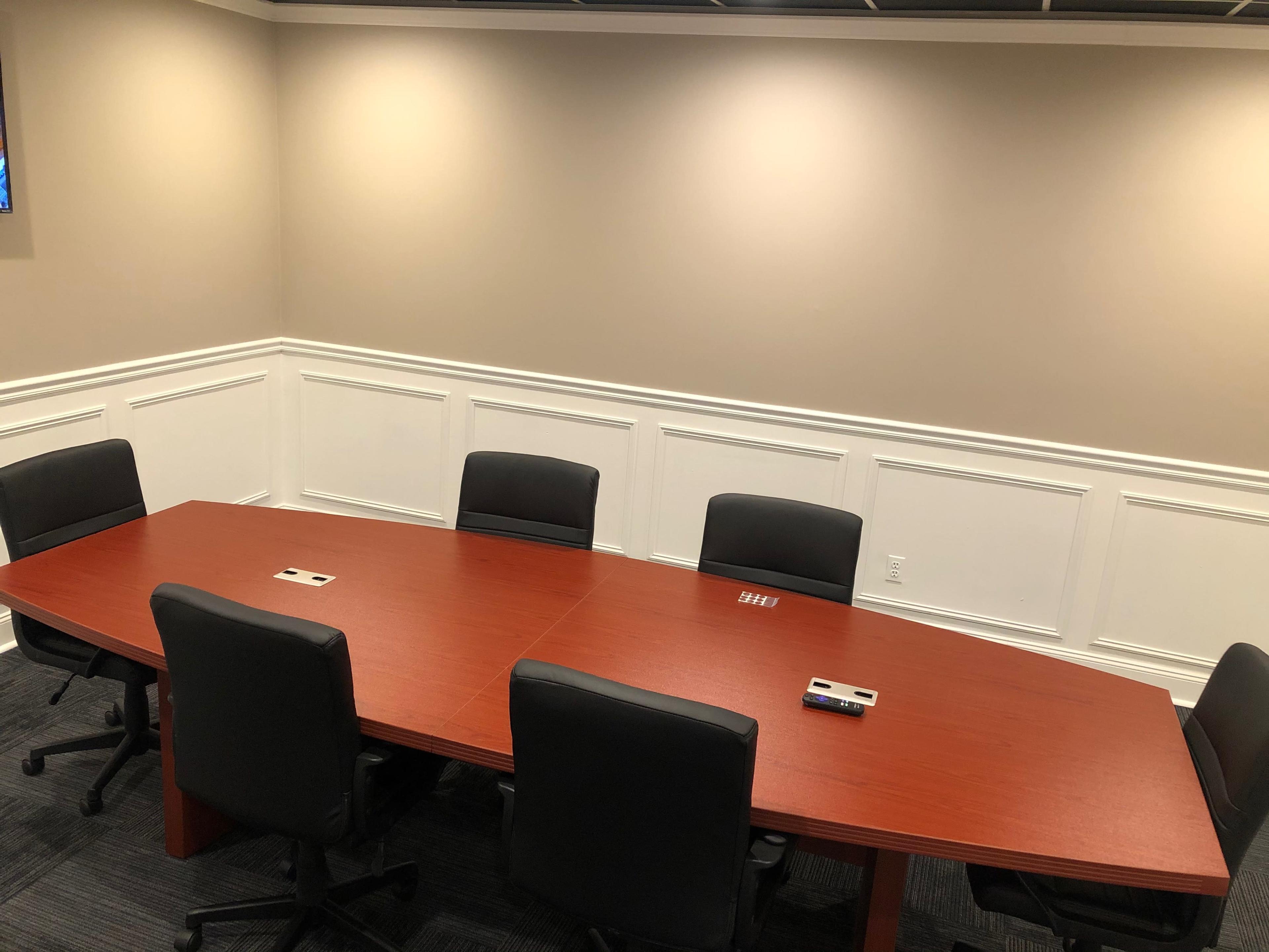 A long, oval wooden conference table is surrounded by six black office chairs in a well-lit meeting room.