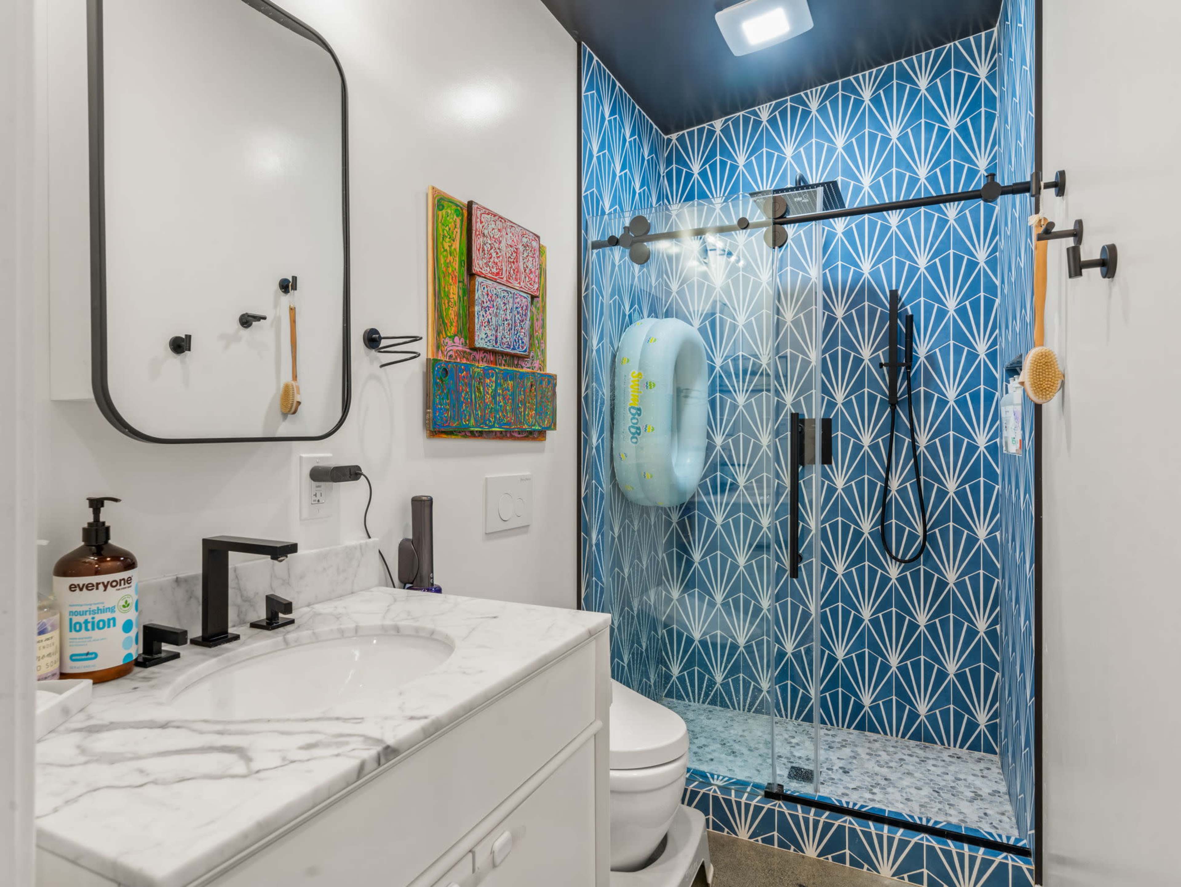 The bathroom features a modern design with a glass shower enclosure, a white vanity with a marble countertop, and a vibrant blue patterned wall behind the shower.