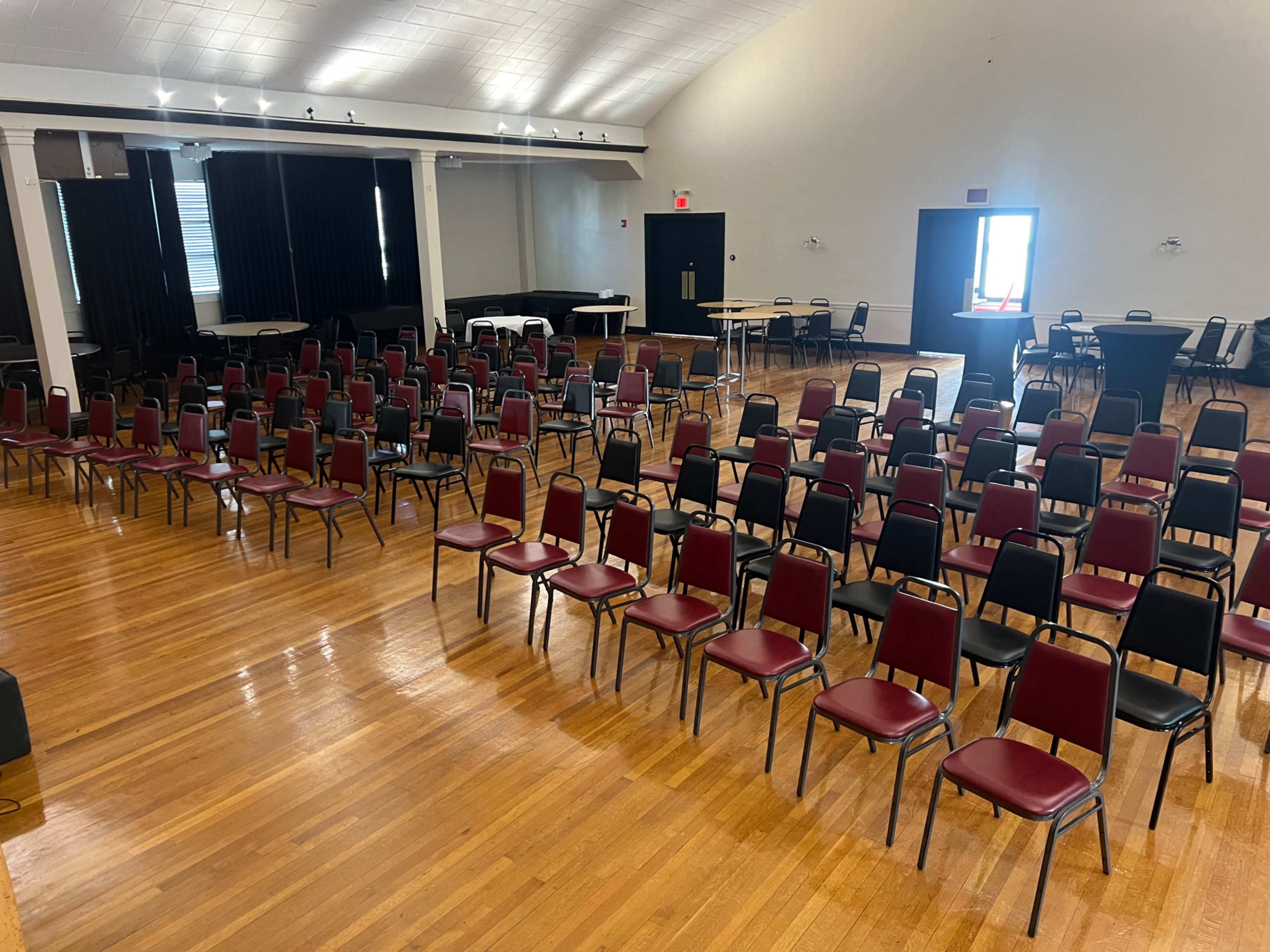 The image shows a large indoor space arranged with rows of empty chairs on a polished wooden floor.