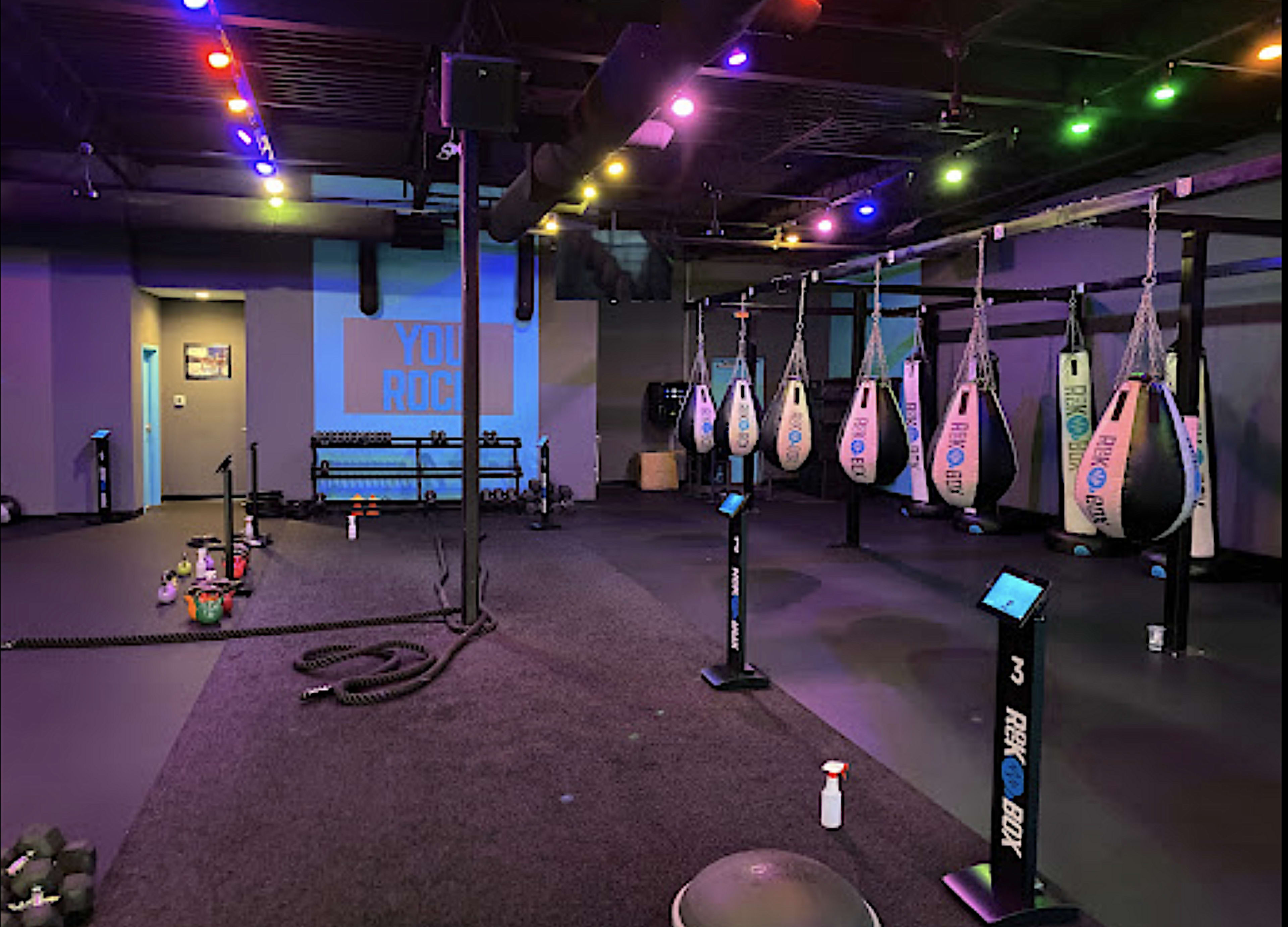 A fitness training area equipped with heavy bags, exercise ropes, and various workout equipment, illuminated by colored lights.