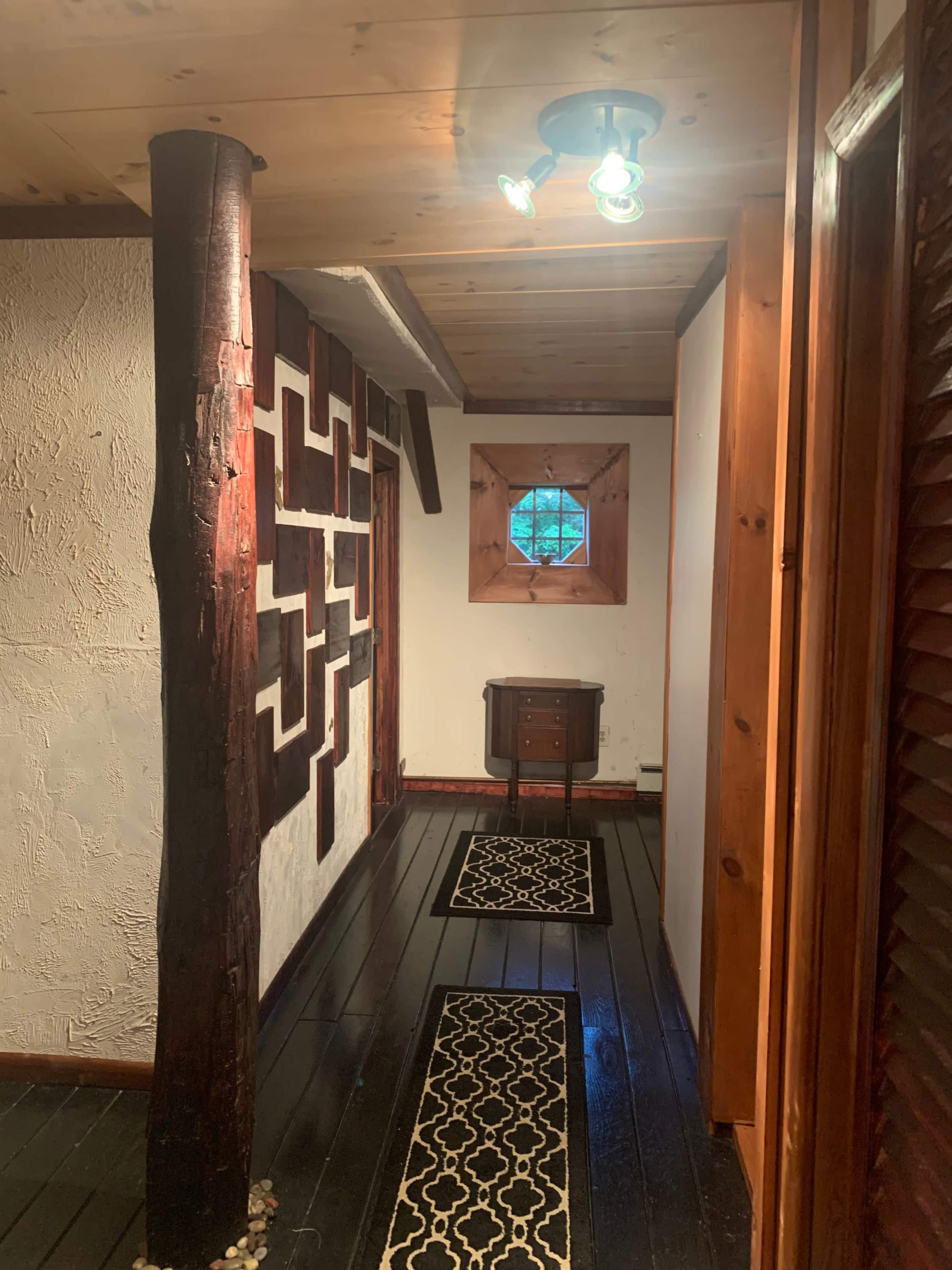 A narrow hallway with wooden walls, a geometric patterned decoration on one side, and a small window at the end.
