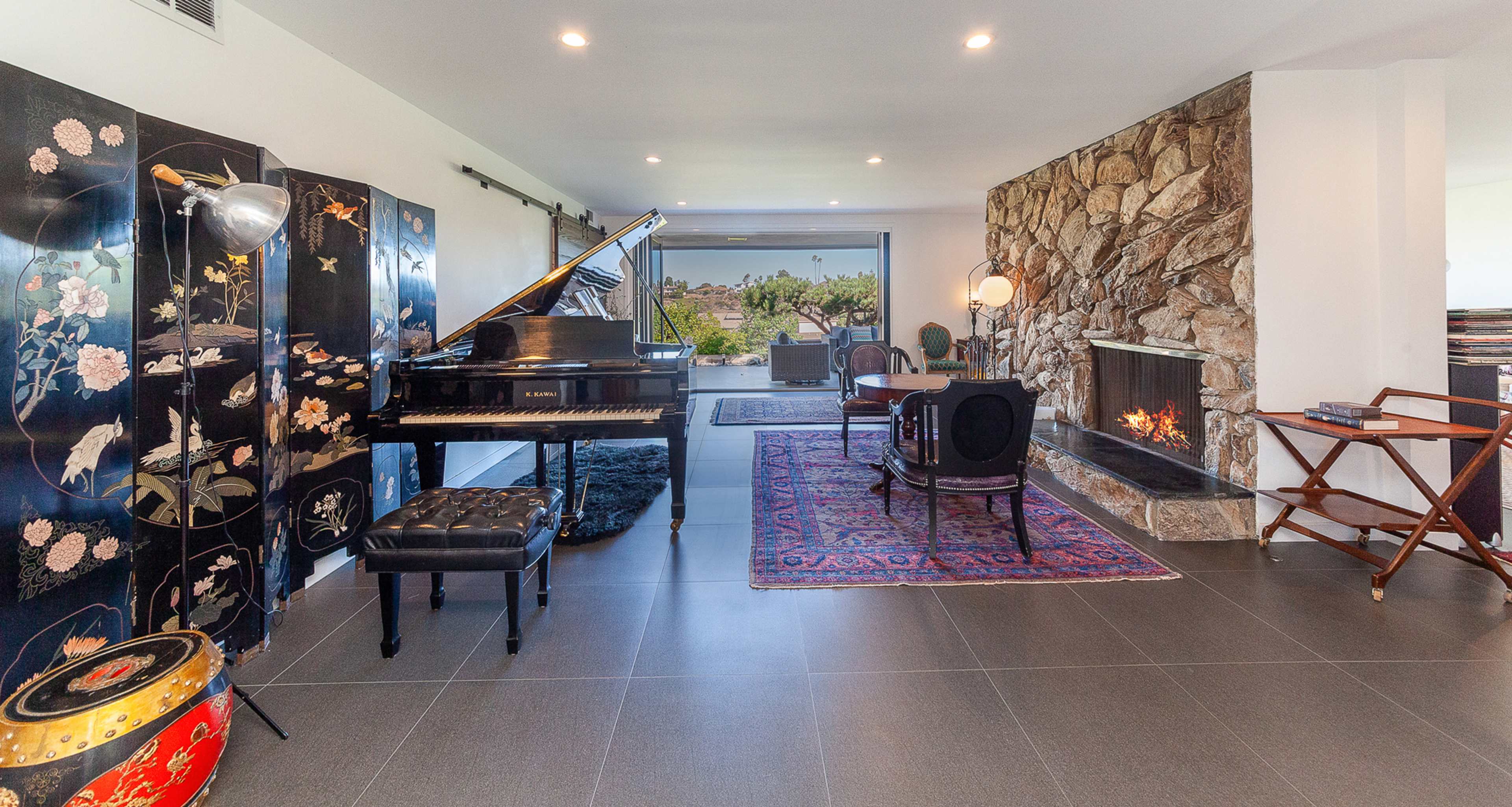 A modern living space featuring a grand piano, a stone fireplace, decorative screens, and a view of the outdoors.