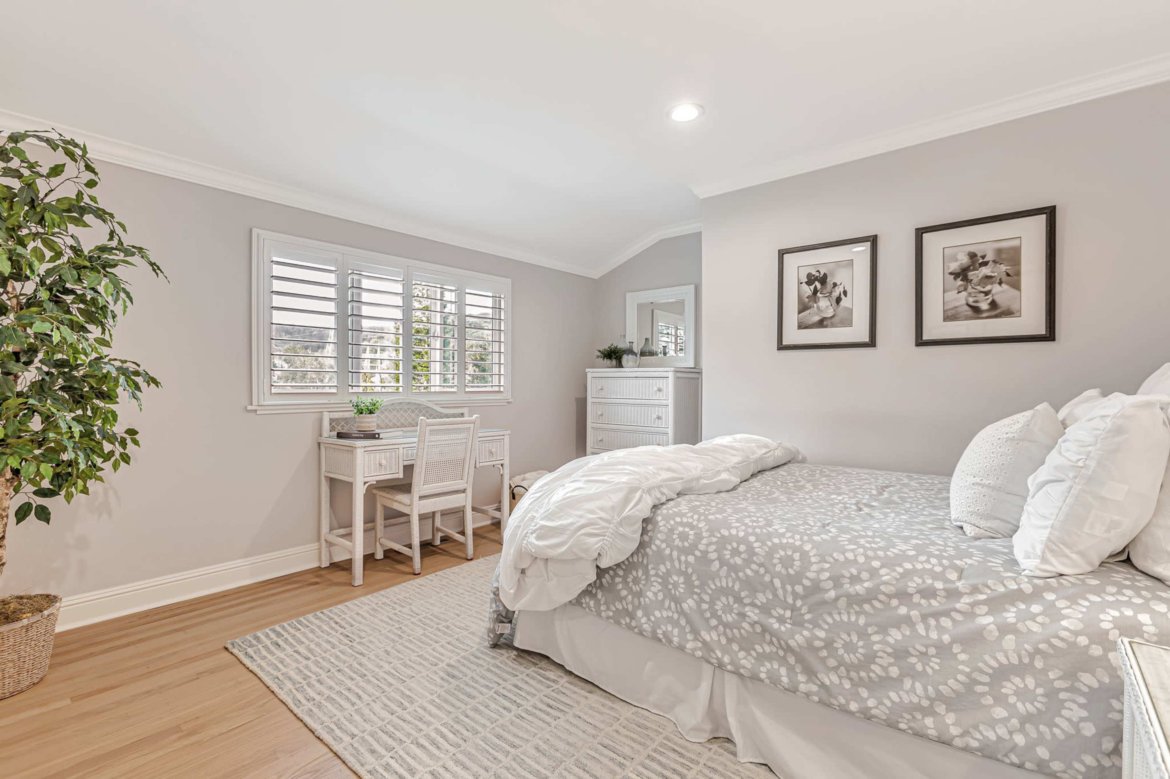 The image shows a bedroom with a bed, a small desk with two chairs, and framed artwork on the walls.
