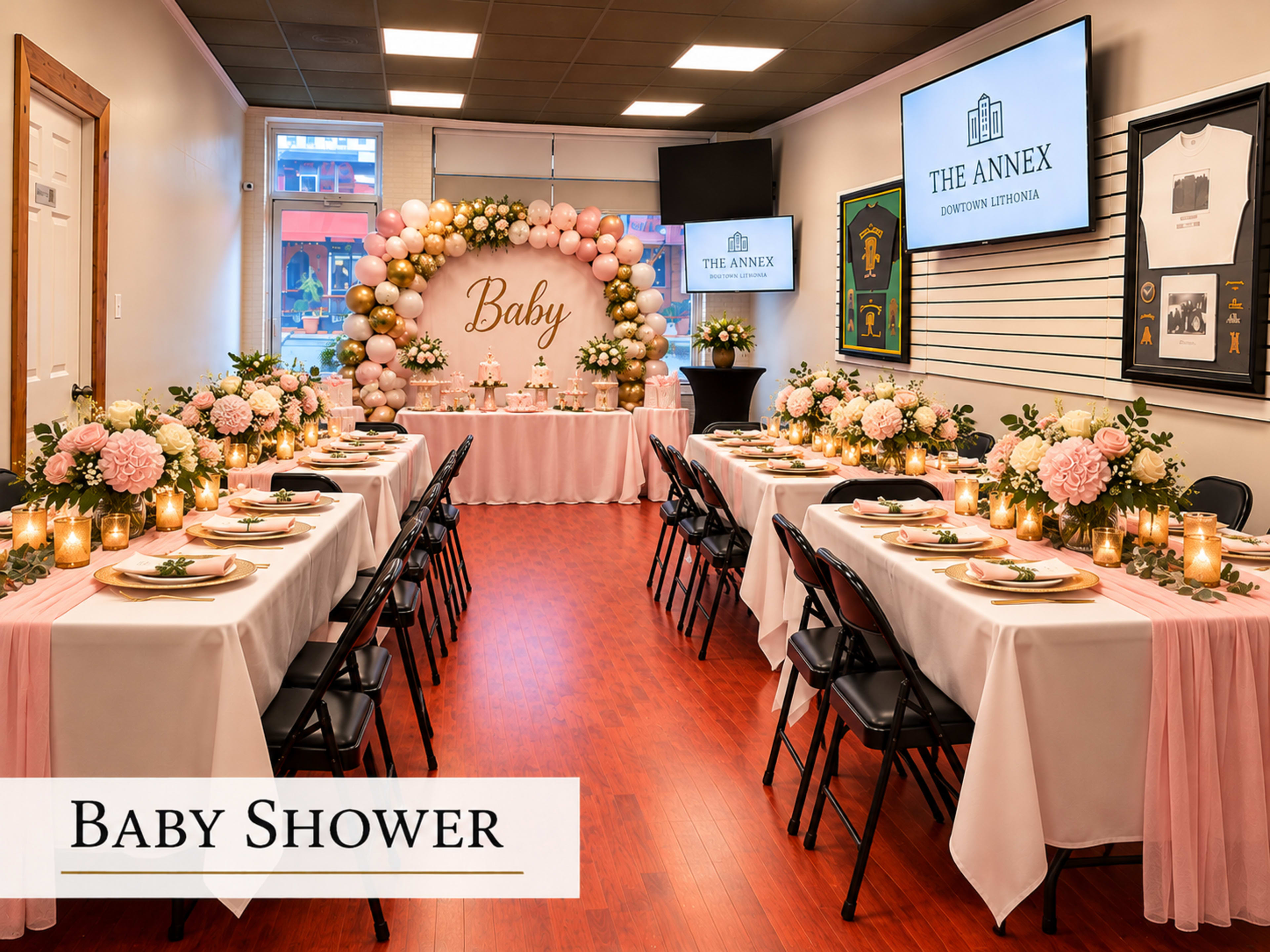 A decorated venue for a baby shower features elegantly set tables with floral centerpieces, candles, and a backdrop displaying the word "Baby."