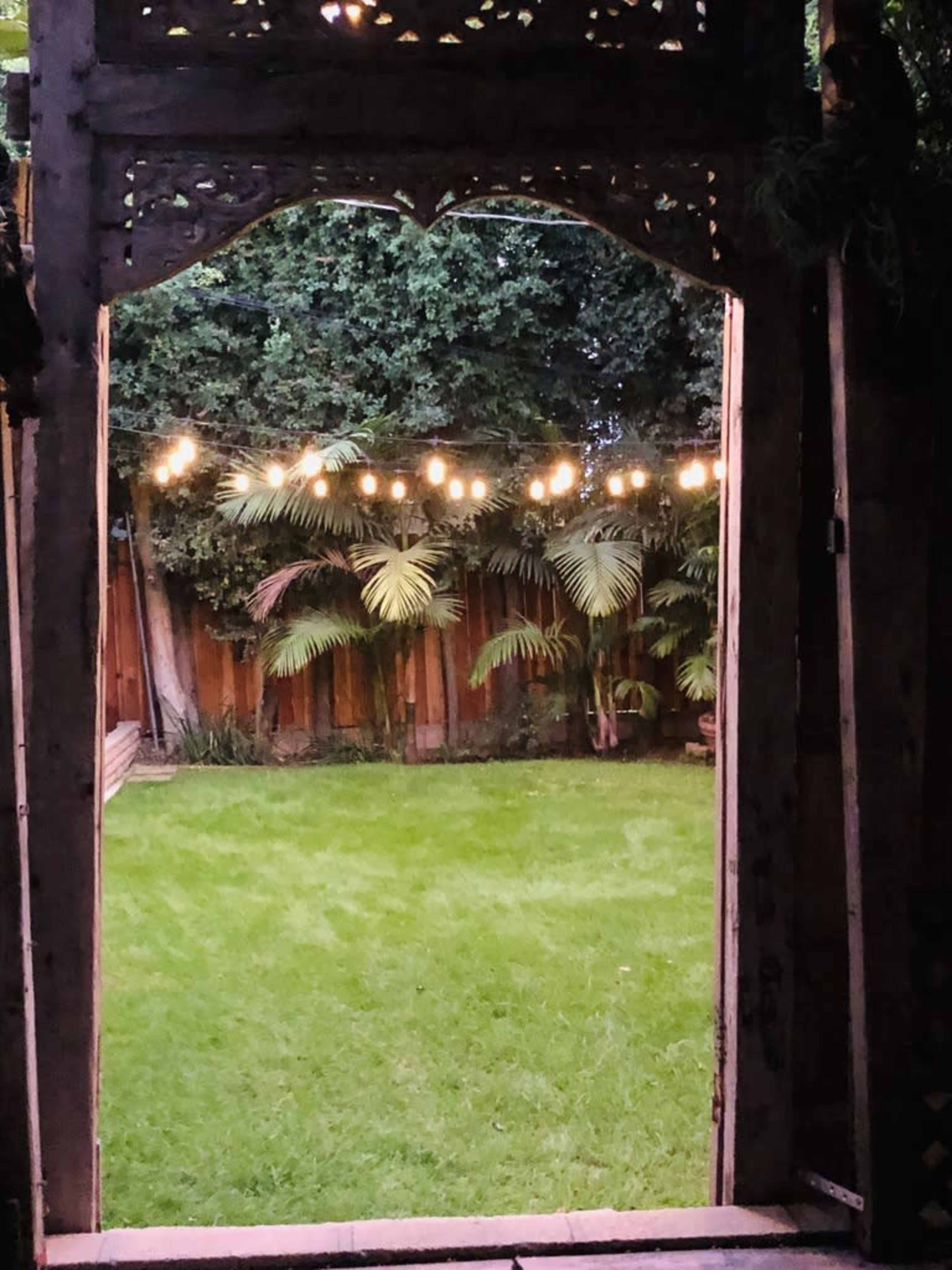 A doorway frames a well-lit backyard with green grass and palm trees under string lights.