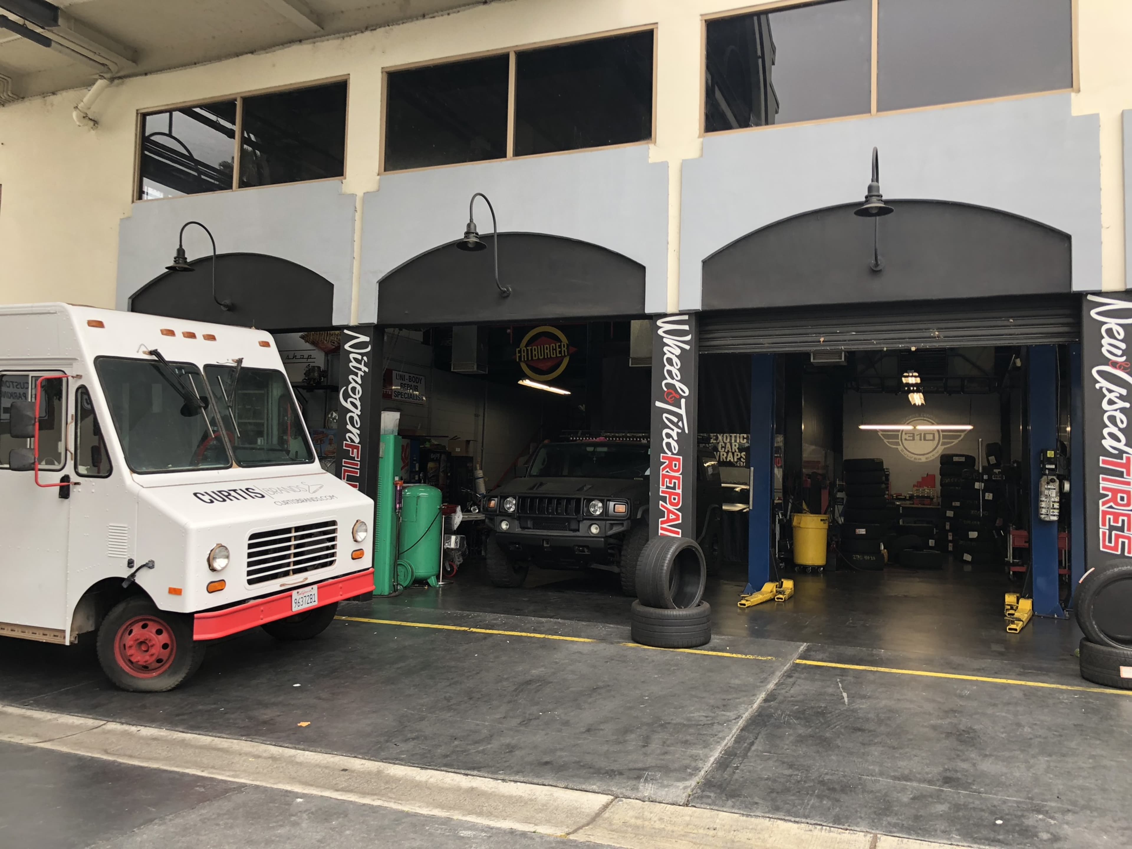 The image shows a service garage with two bays, one containing a vehicle and the other featuring a food truck parked outside.