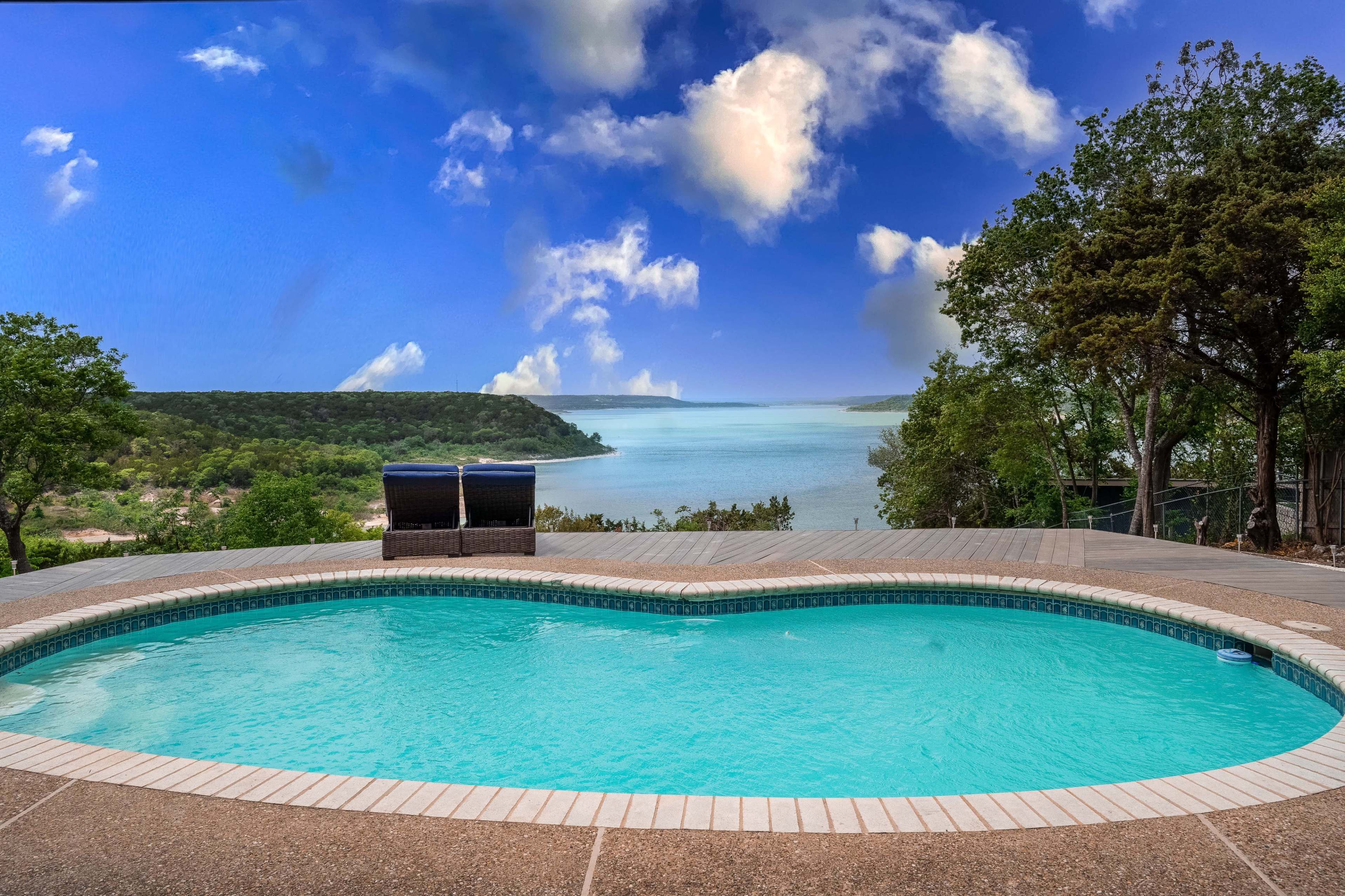 A heart-shaped swimming pool overlooking a lake and wooded shoreline under a blue sky with clouds.