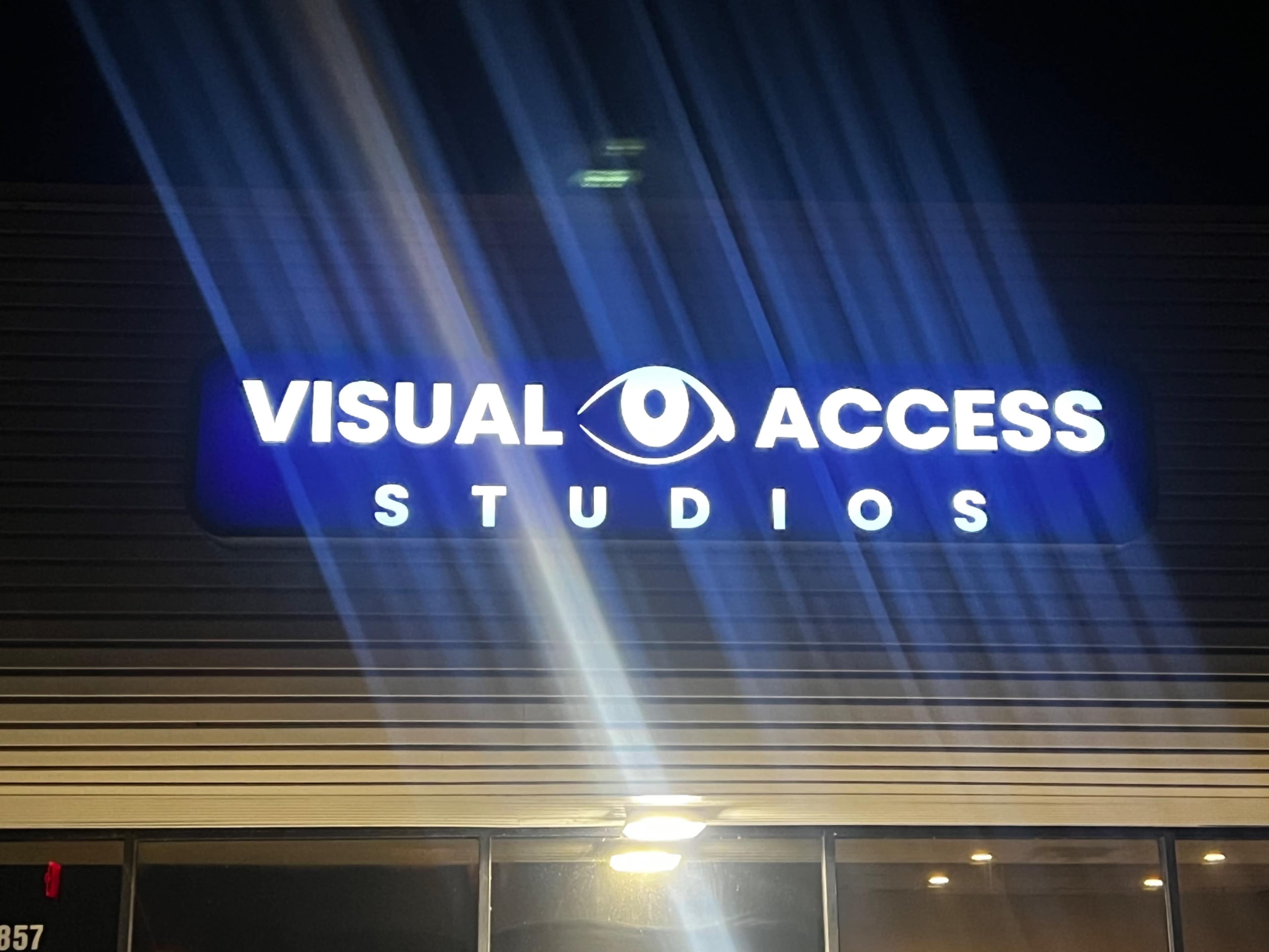 A sign for "Visual Access Studios" illuminated at night, featuring an eye graphic above the name.