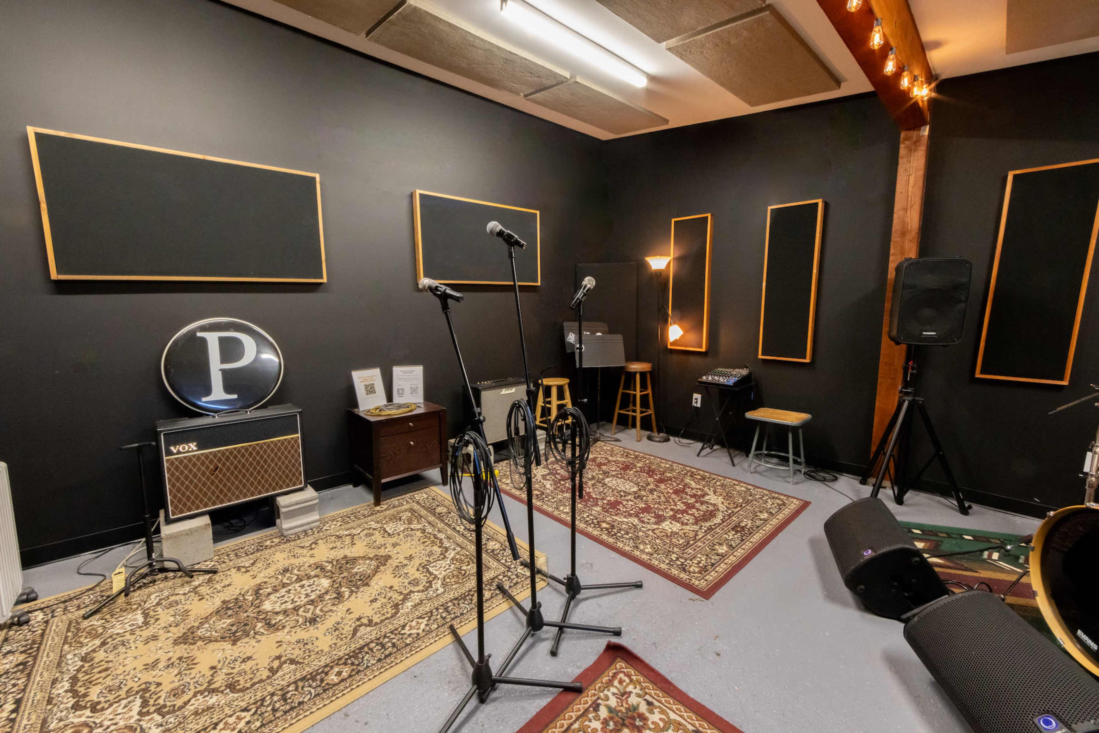 A music rehearsal room with microphones, sound equipment, and patterned rugs on a concrete floor.