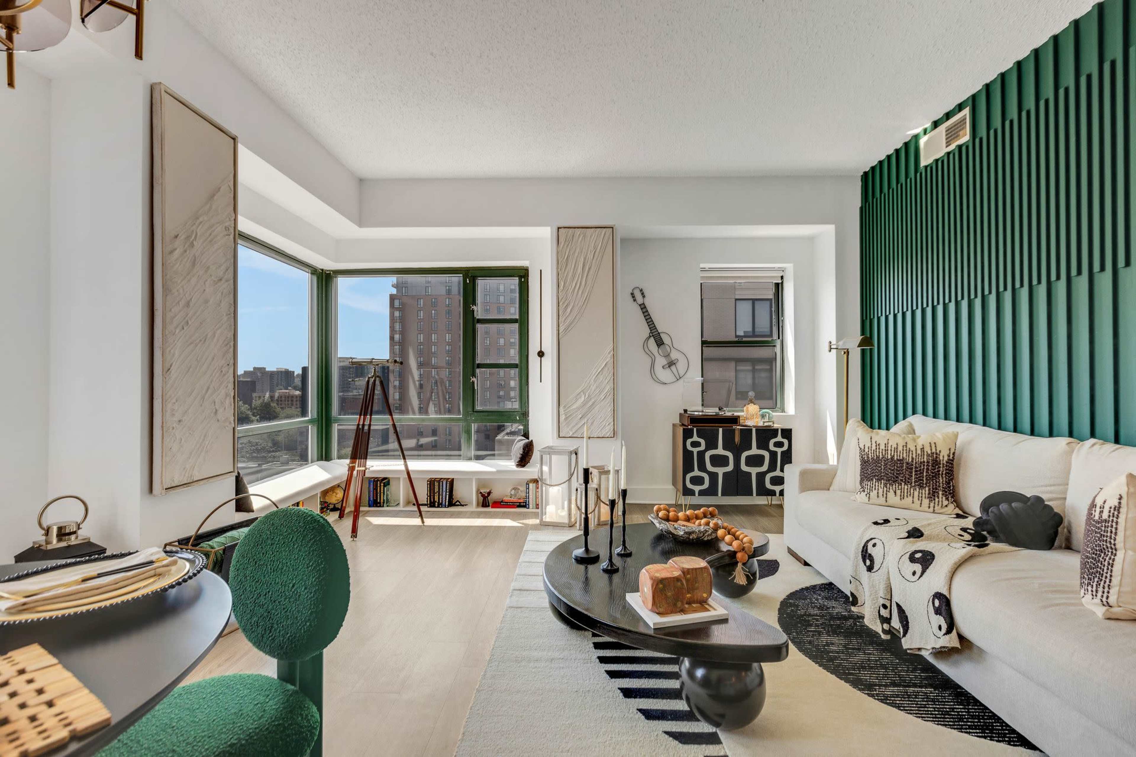A modern living room with a sectional sofa, a large window offering a city view, and green accent walls.