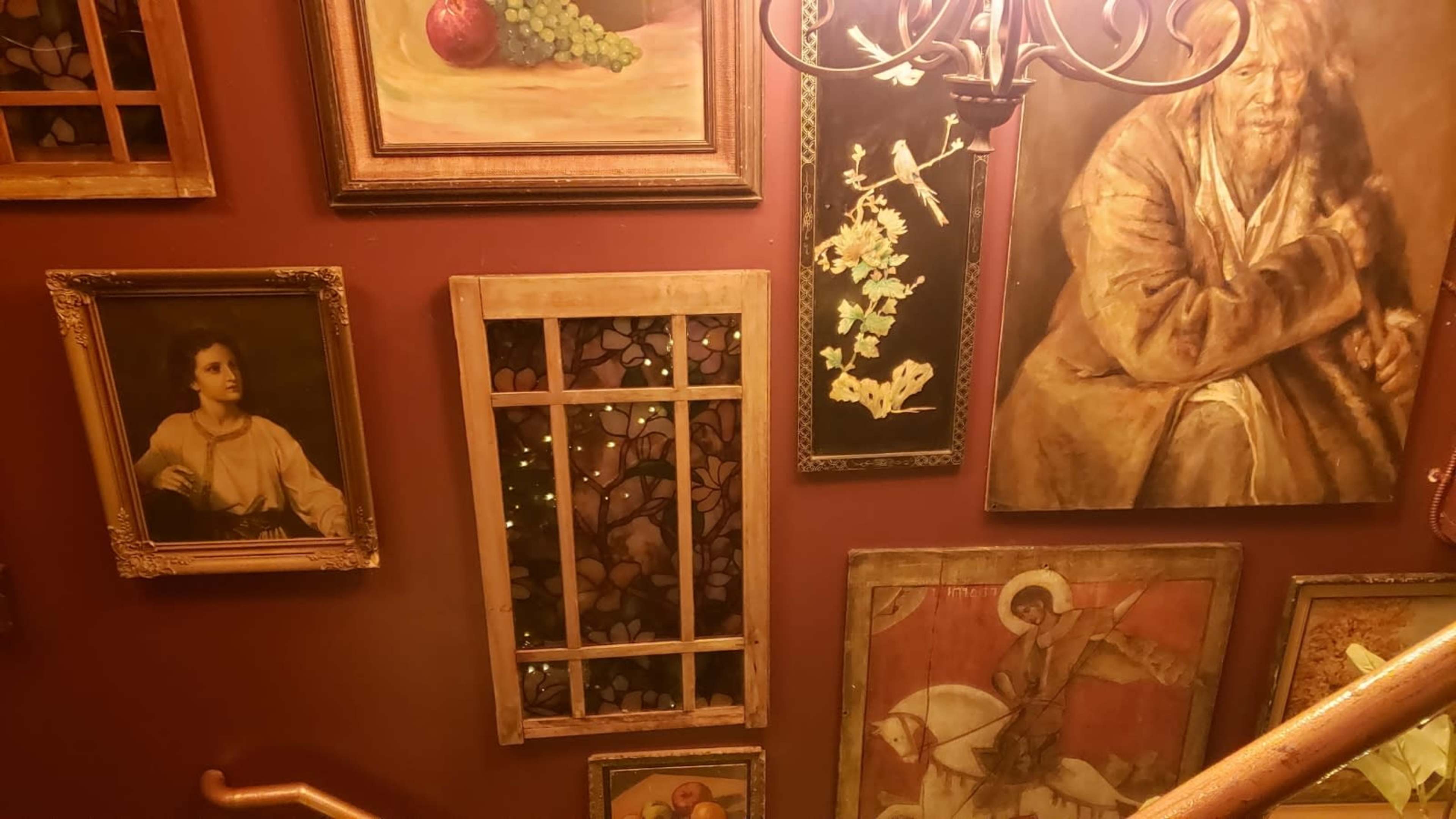 The image shows a staircase wall adorned with various framed paintings and decorative elements, illuminated by warm light.