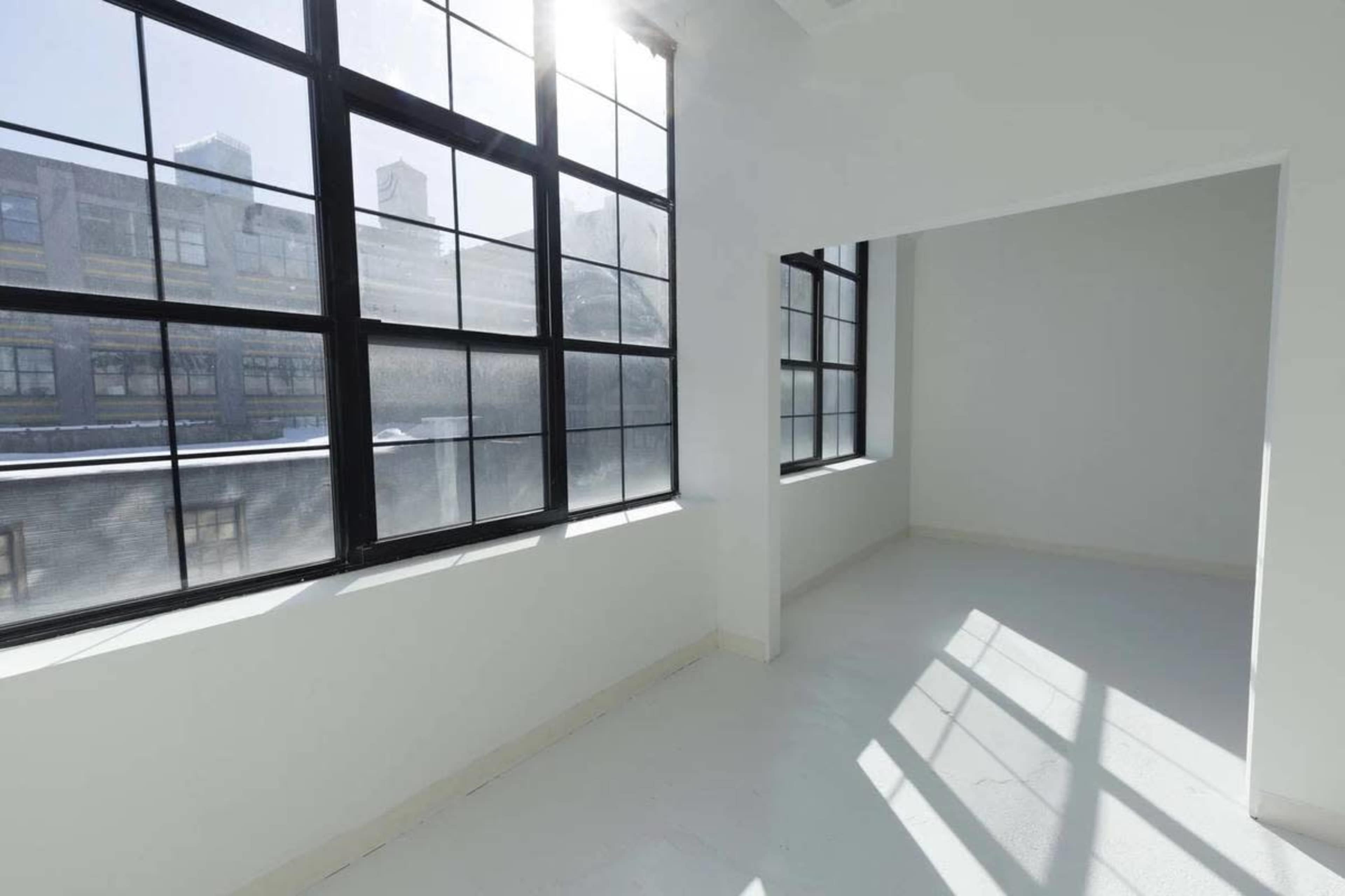 The image shows a bright, empty room with large windows and white walls, casting shadows on the floor.