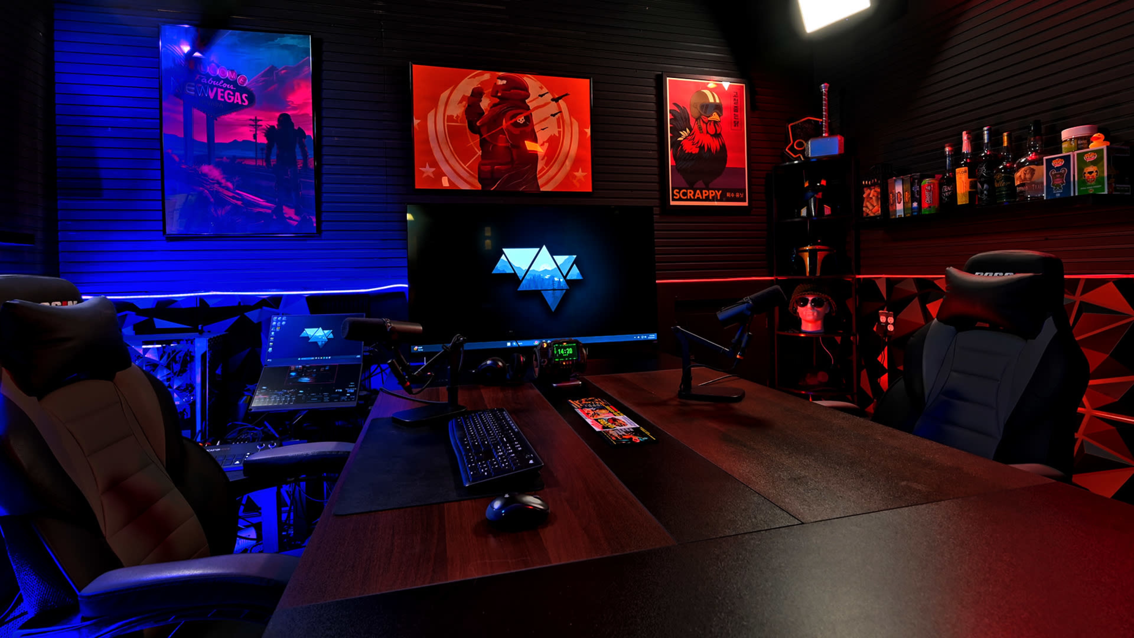 The image shows a modern gaming or streaming setup with two ergonomic chairs, a large monitor displaying a logo, and colorful ambient lighting on the walls.