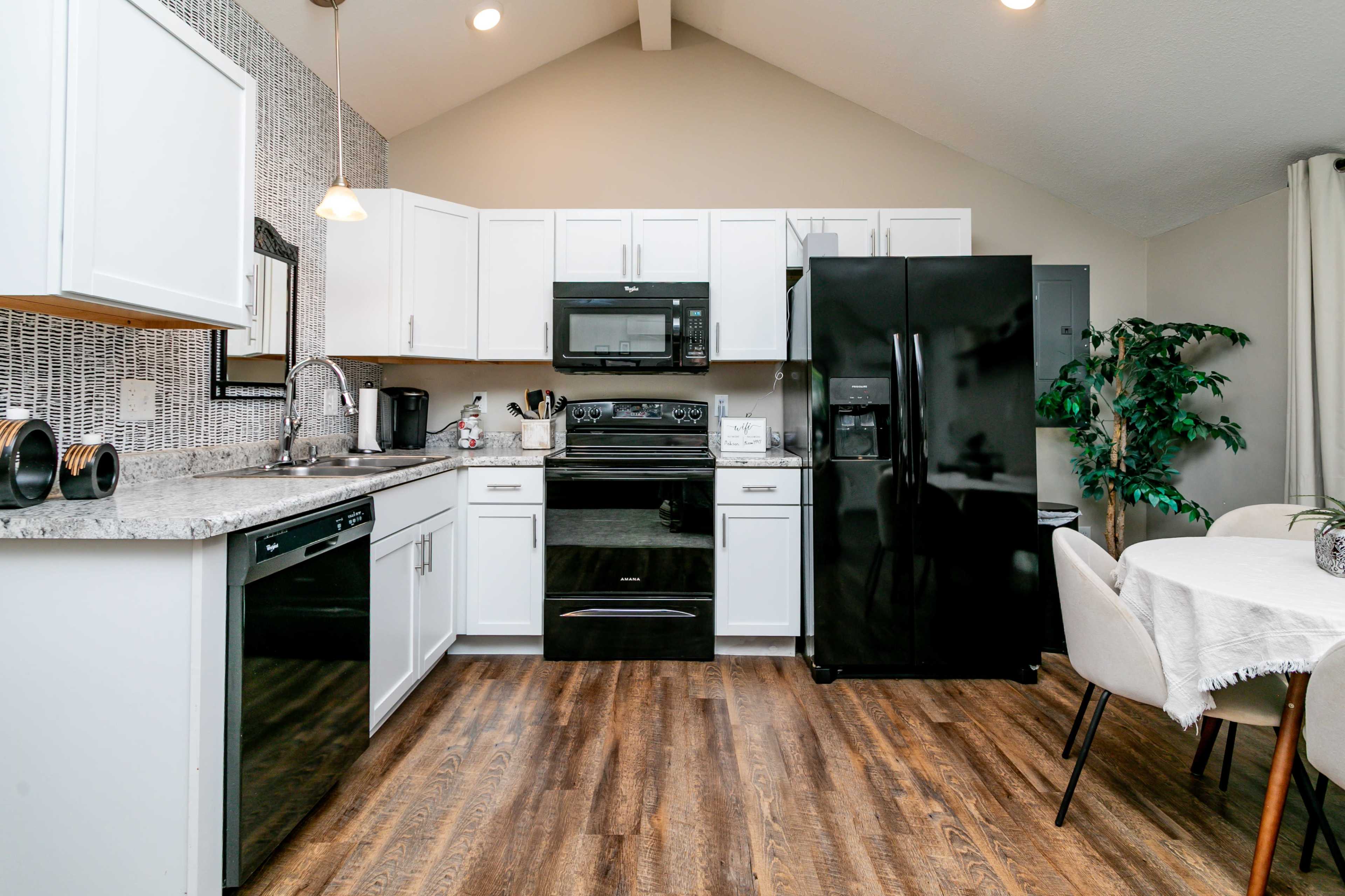 The image shows a modern kitchen with white cabinets, black appliances, and a wooden floor.