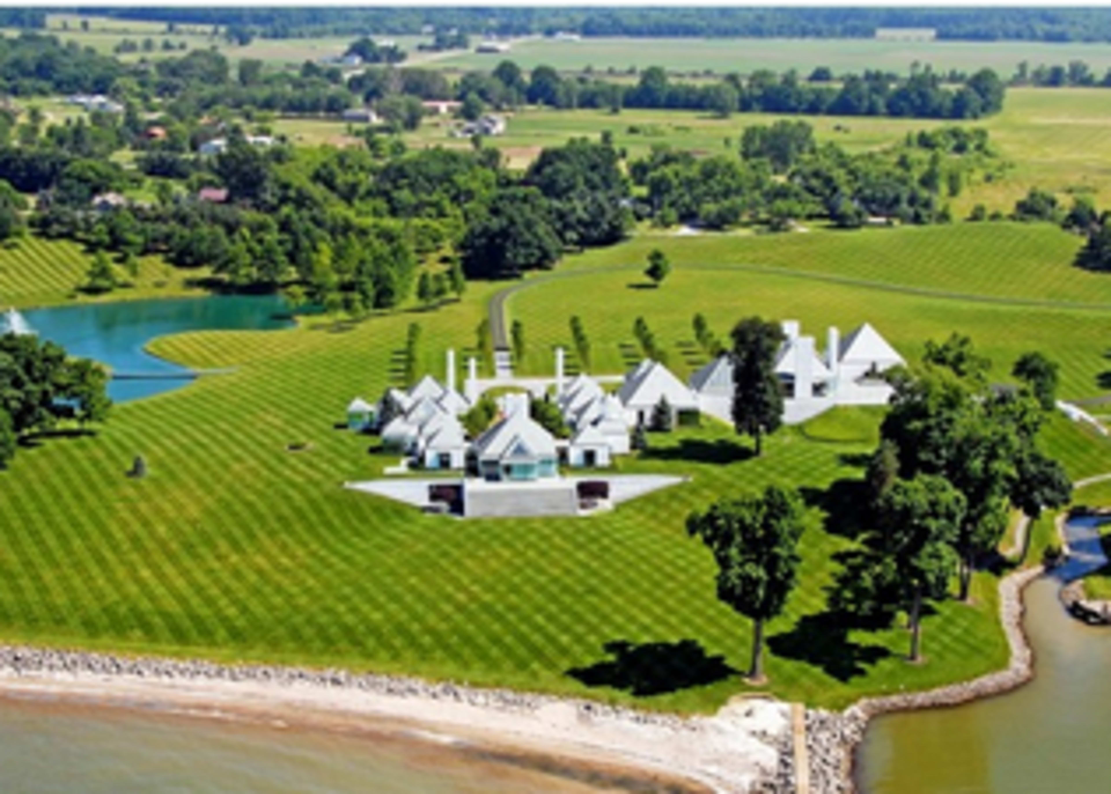 The image shows an expansive estate with modern architecture, neatly manicured lawns, and a waterway, set in a rural landscape.