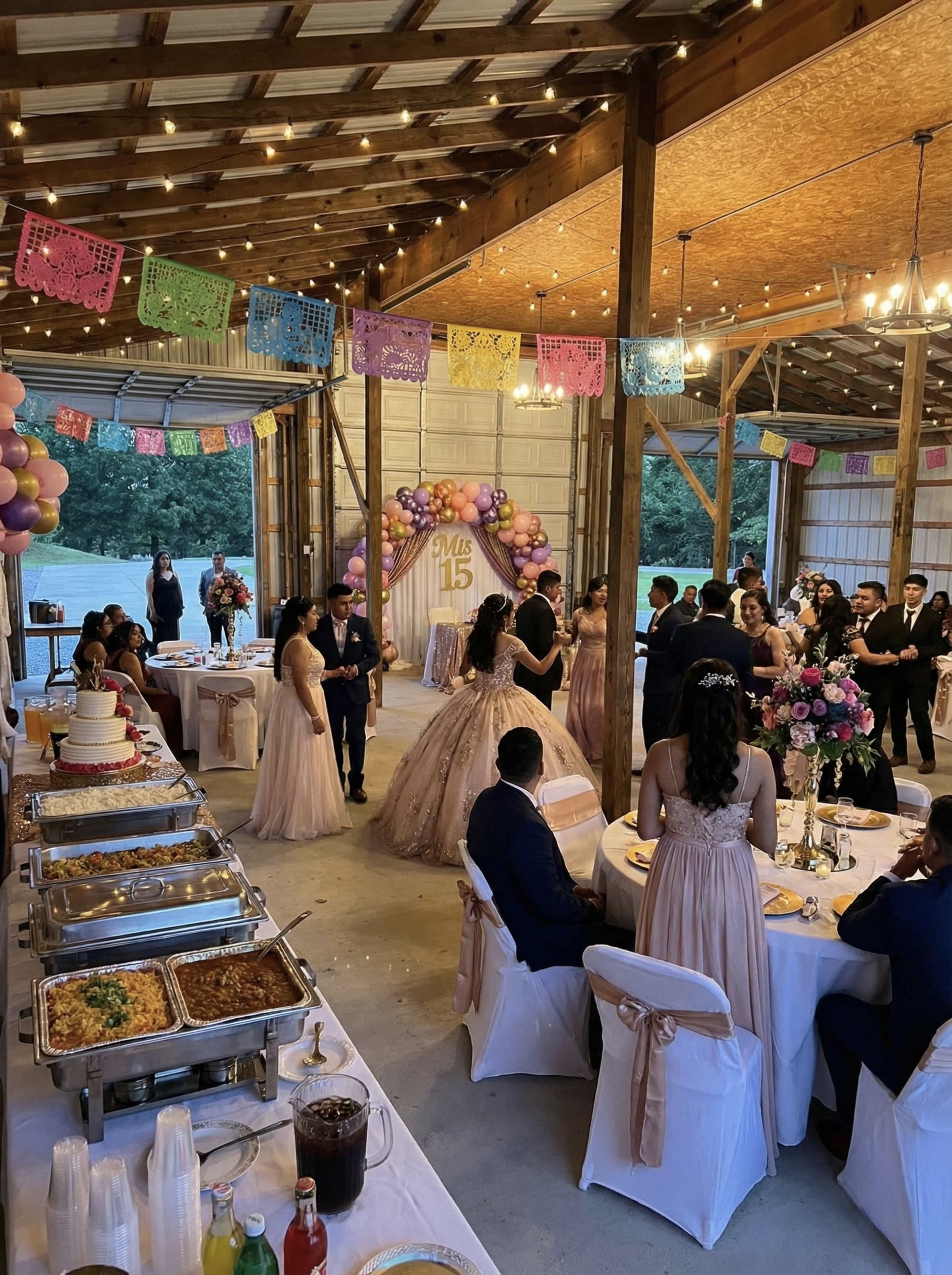 The image depicts a festive indoor event with elegantly dressed guests gathered around tables adorned with food and decorations, celebrating a quinceañera.
