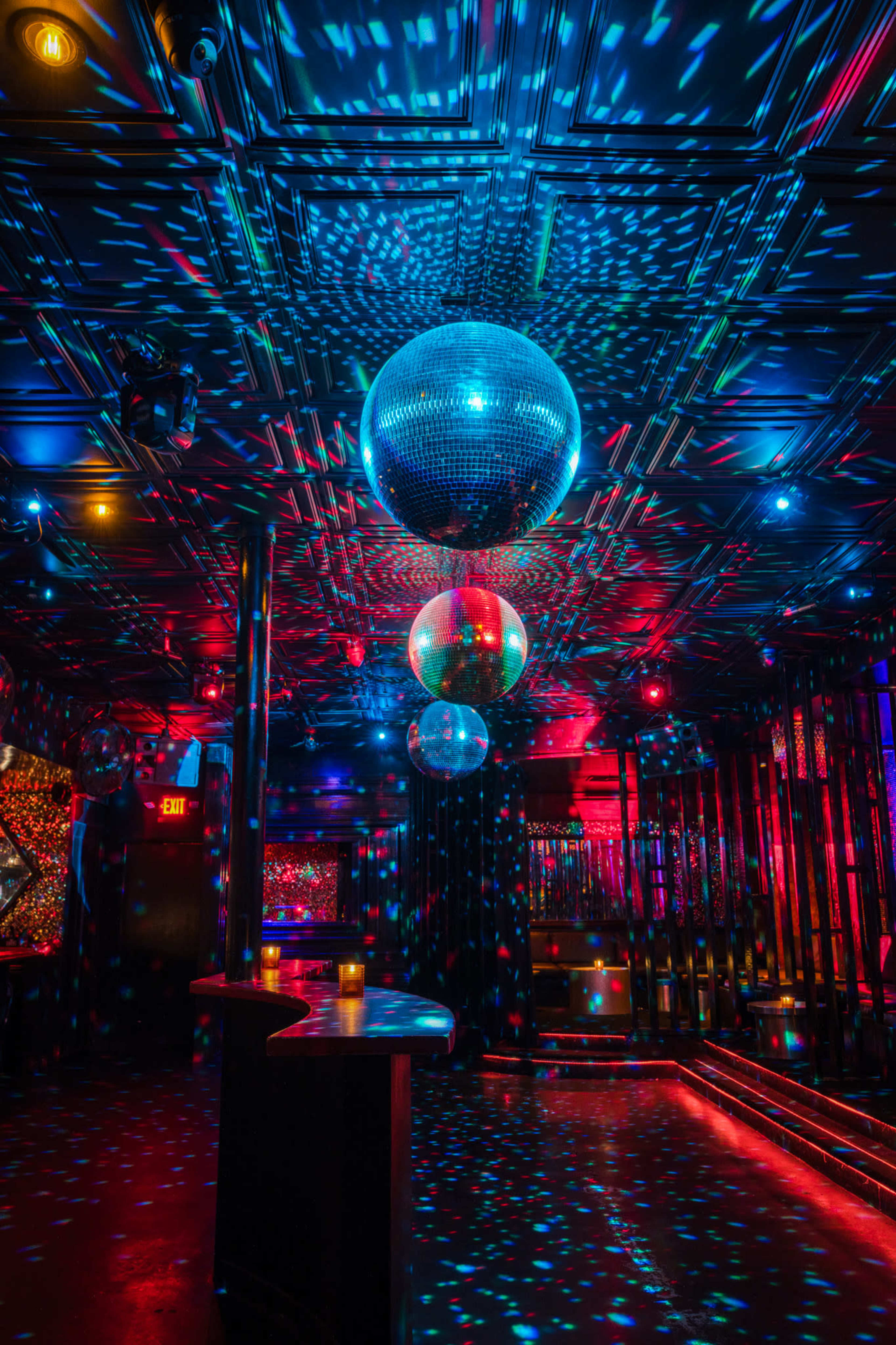 A dimly lit nightclub interior featuring multiple disco balls and colorful light patterns projected on the floor and walls.