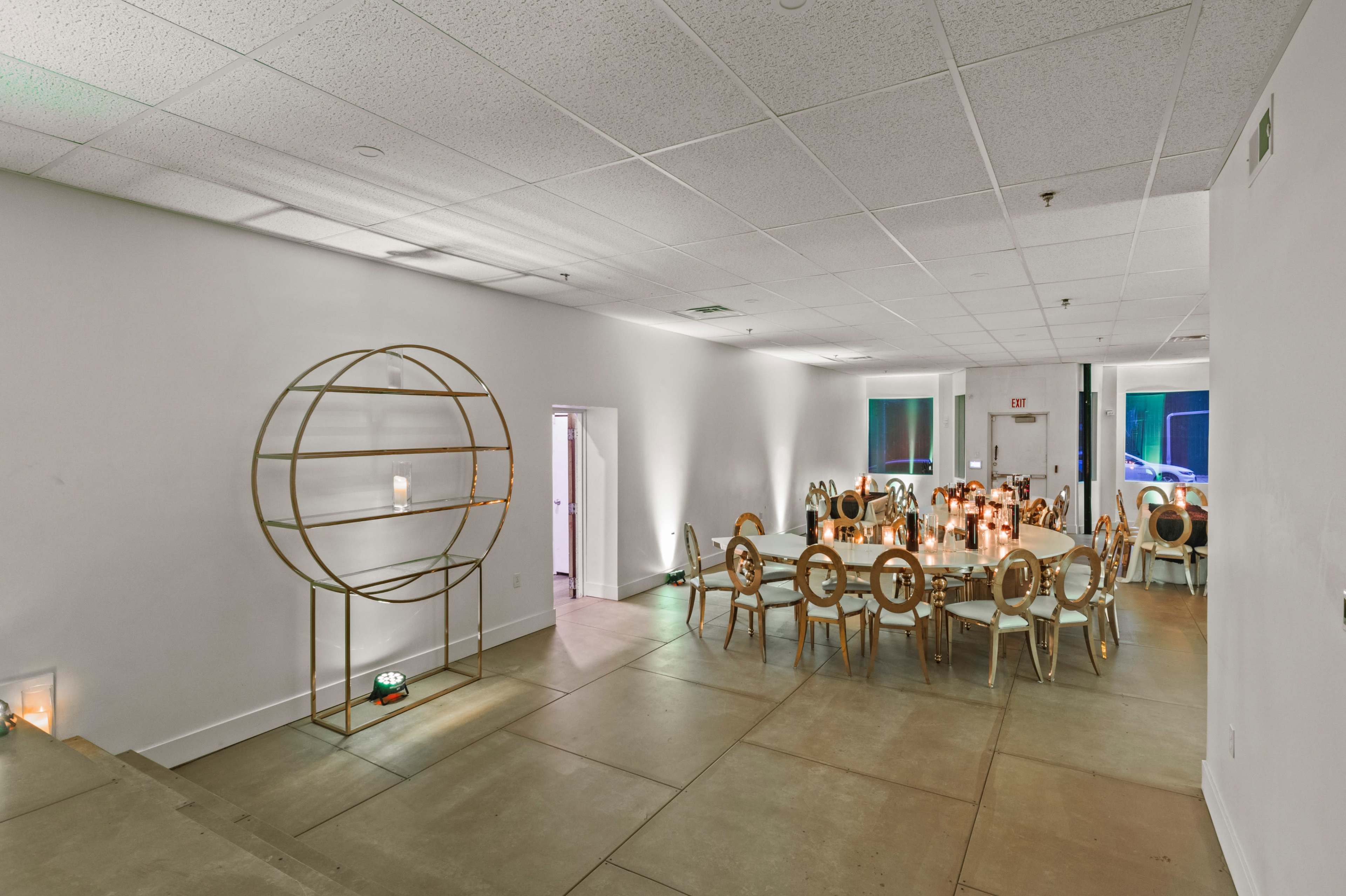 A spacious, well-lit event room with a large dining table surrounded by chairs and a decorative gold shelving unit on the side.