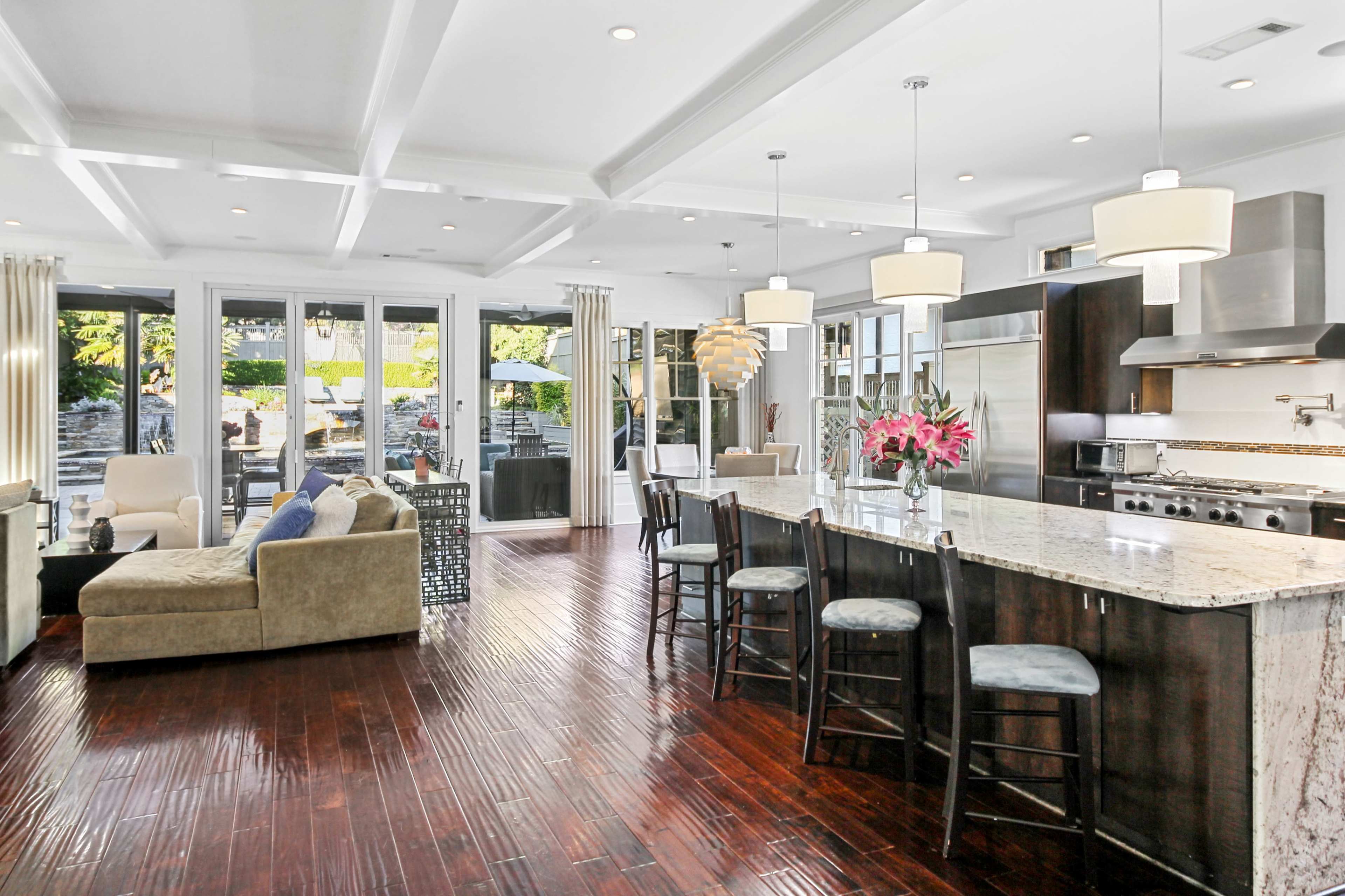 A modern kitchen and living area feature an island bar with seating, large windows, and a cozy seating arrangement.
