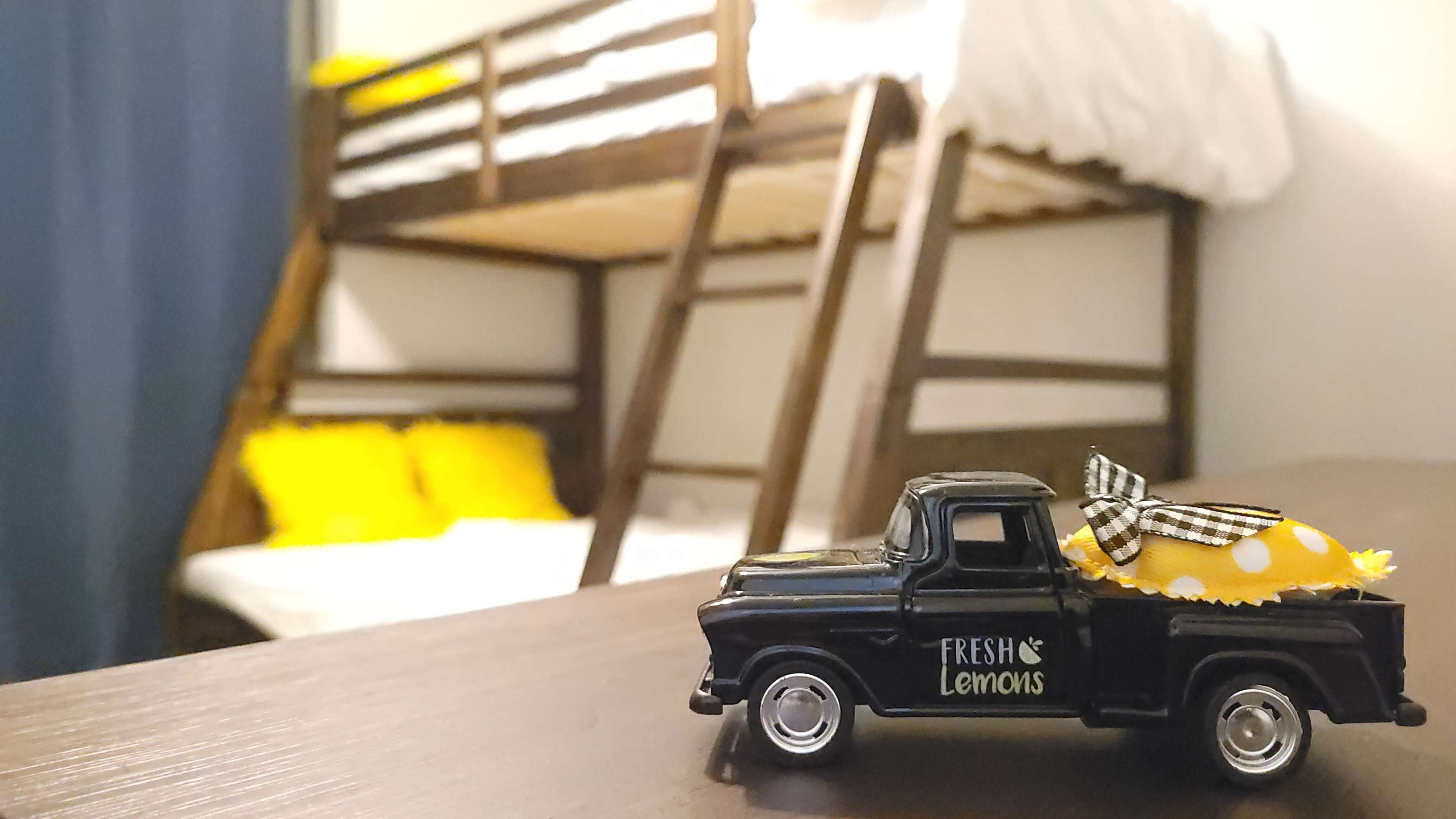 A small black toy truck with a decorative bundle sits on a wooden surface in a room featuring a bunk bed in the background.