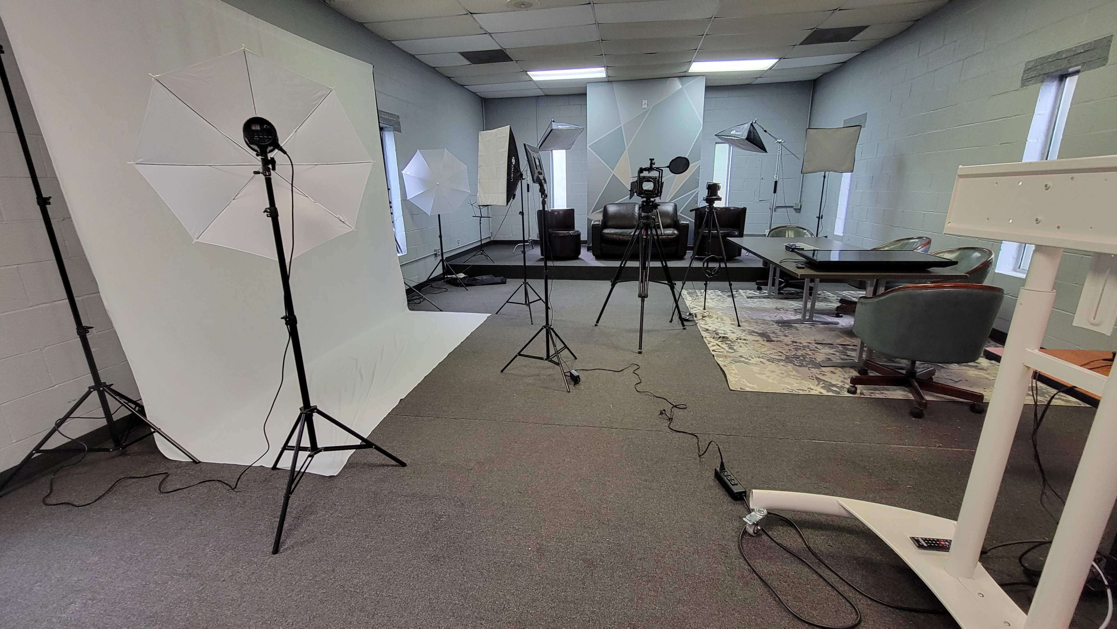 A photography studio setup with multiple lights, tripods, and a large table in a room with gray walls and carpet.