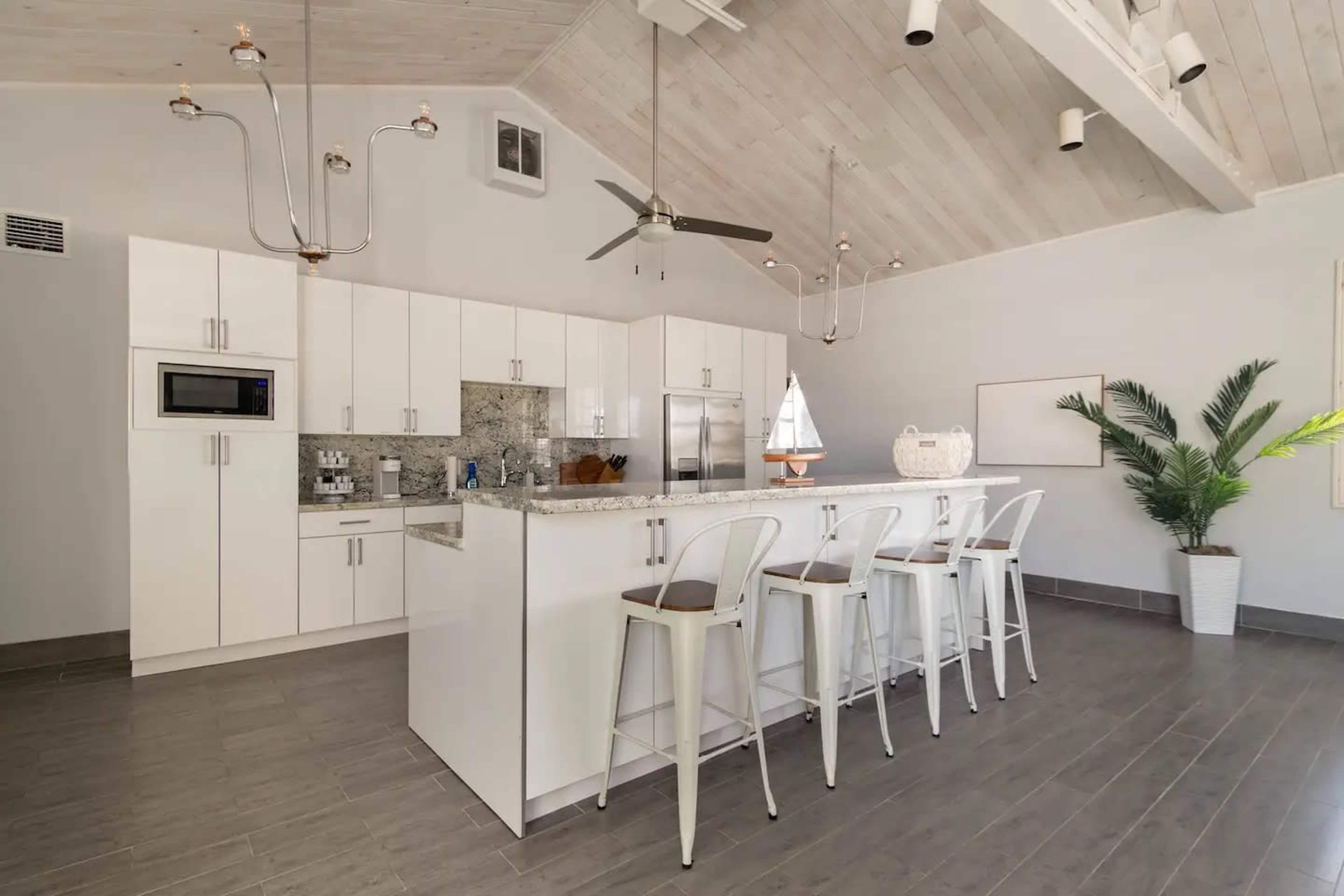 A modern kitchen features white cabinetry, gray flooring, and a spacious island with bar stools.