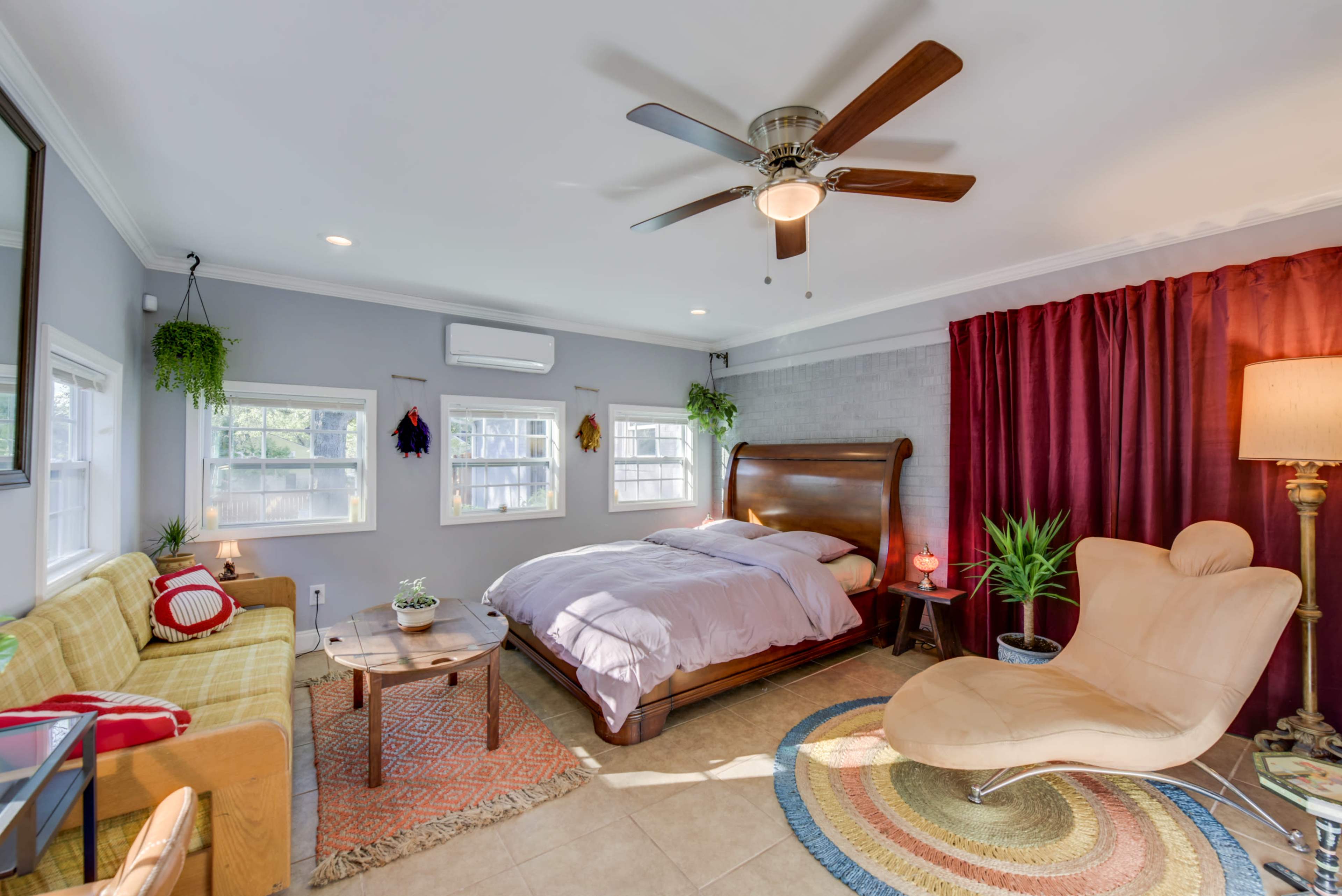A cozy bedroom featuring a large wooden bed, a comfortable armchair, a small table, and large windows with natural light.